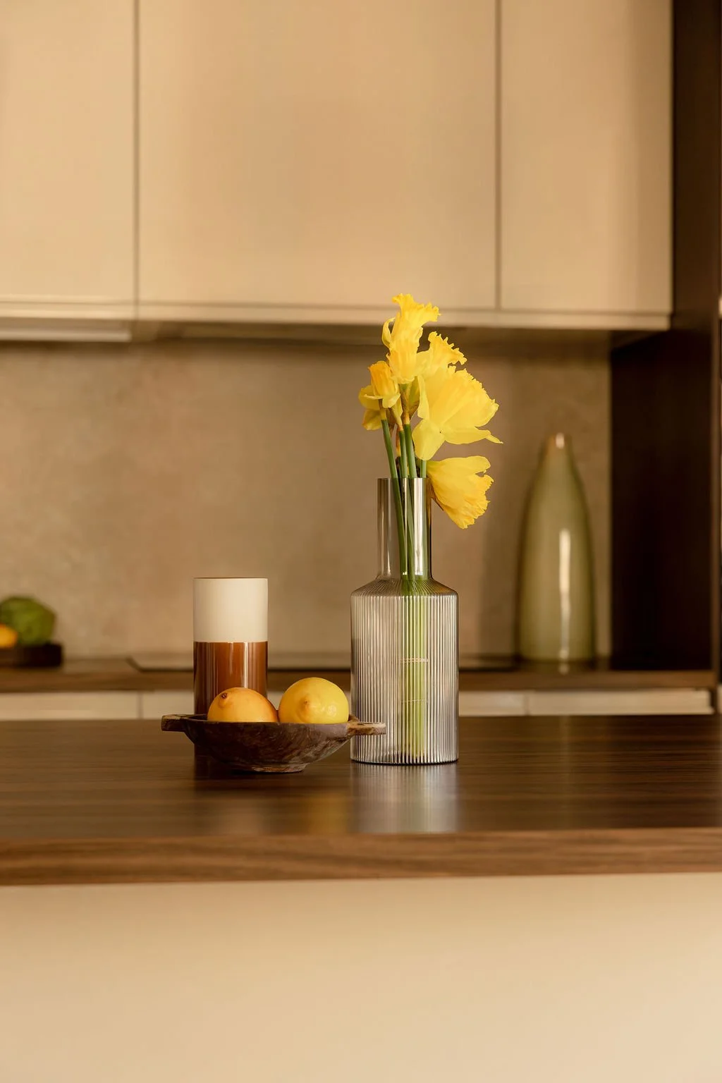 Vase en verre transparent avec des fleurs jaunes, bol en bois avec deux pommes, bougie dans un porte-candles, décor moderne de cuisine.
