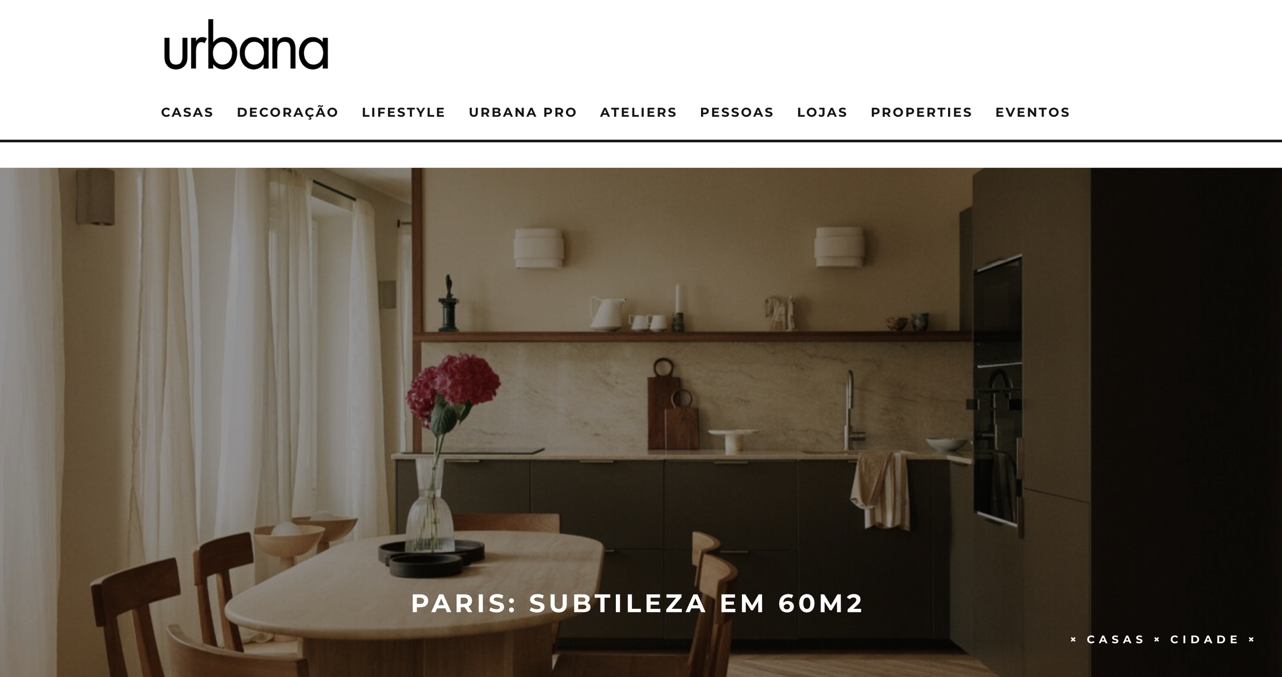 Intérieur d'une cuisine élégante avec un mur beige, des rideaux blancs, une table avec une vase de fleurs et des chaises en bois.