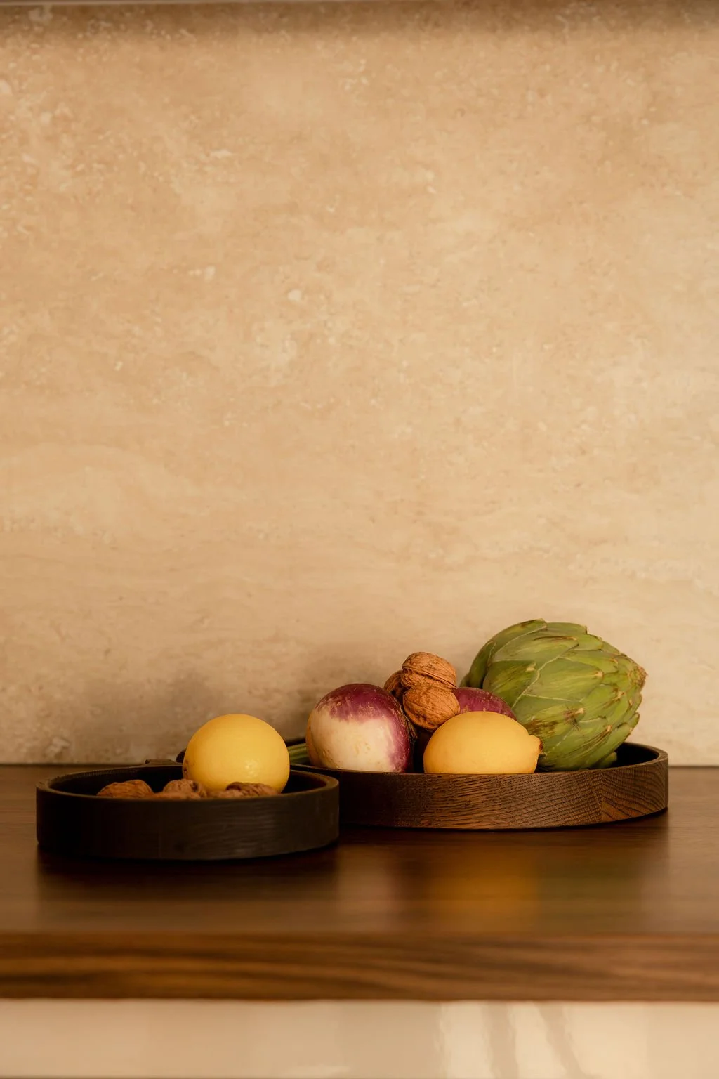 Plateau en bois avec oignons, artichaut, noix, et pommes de terre. Fond beige avec texture douce.