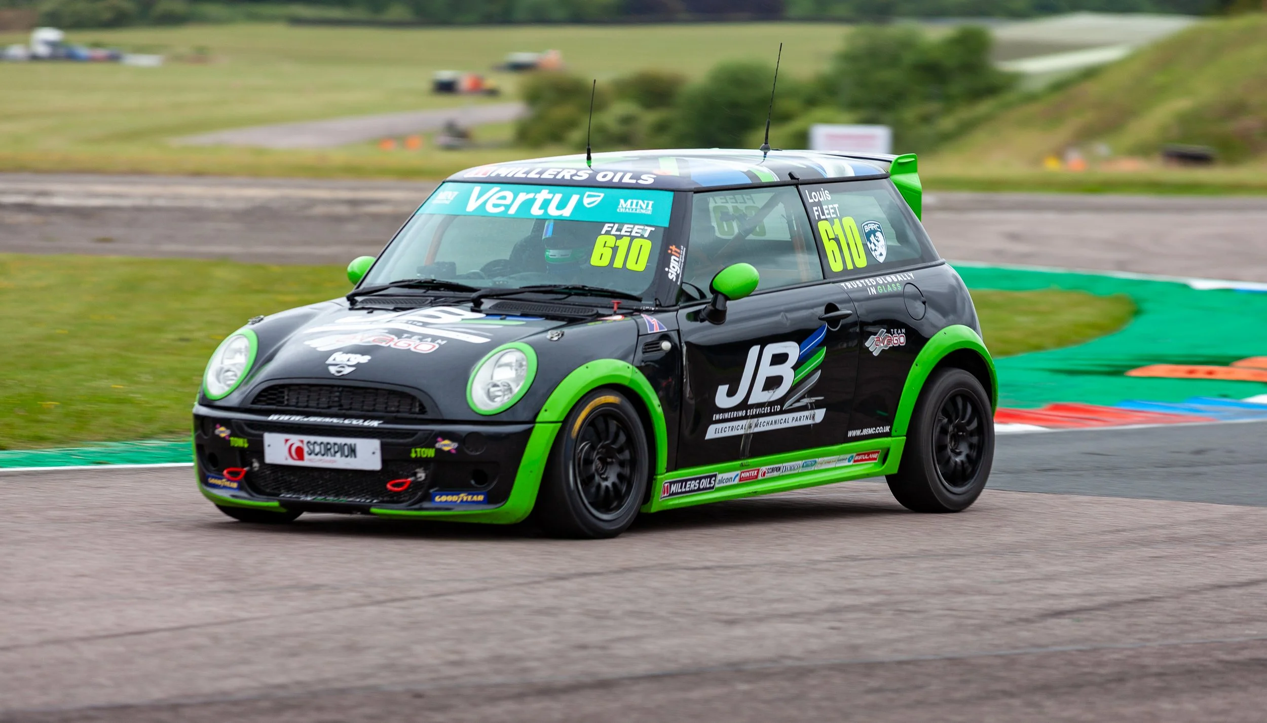 A black and green race car on a racetrack with a grassy background.
