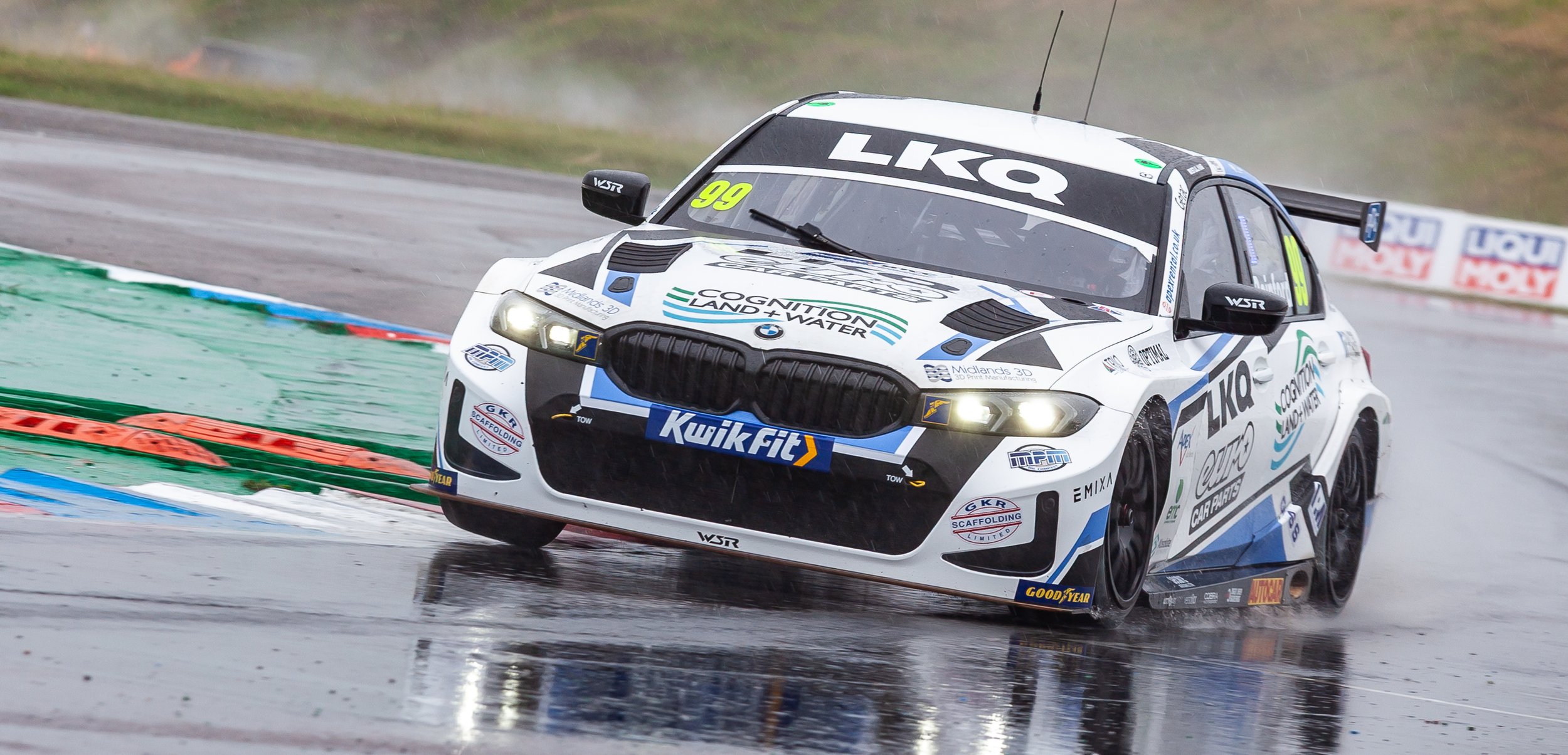 Race car on wet track with rain spray, numbers 99, sponsored by LKA and Kwik Fit.