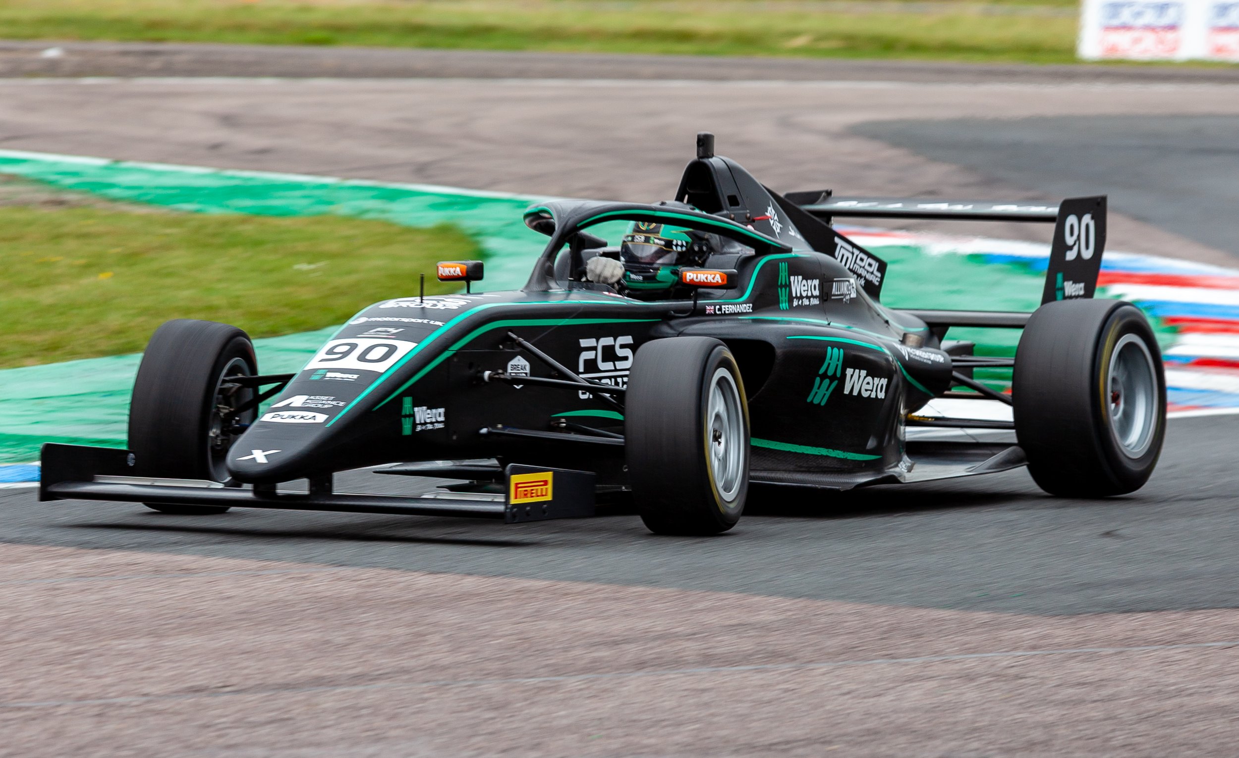 A black Formula race car with the number 90 on the front and side, racing on a track with green and blue curbing.