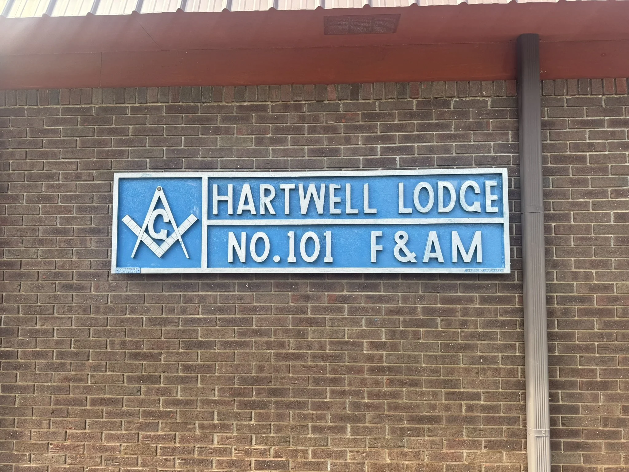 Blue sign on brick wall reads 'Hartwell Lodge No. 101 F & A M' with Masonic symbols.