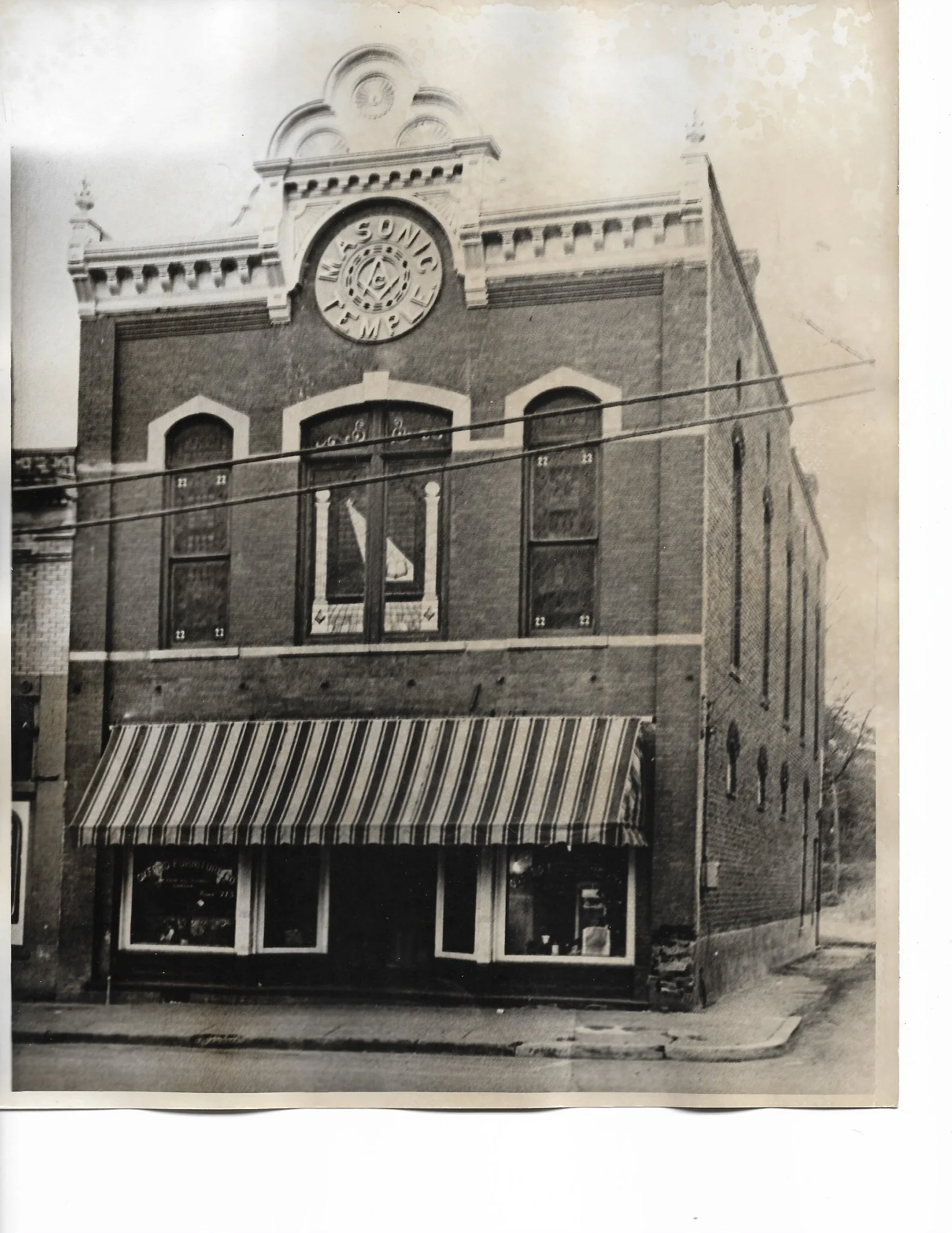 Black and white photo of an old brick building with a striped awning over the storefront and a decorative facade on the upper part, featuring a circular sign that reads 'Sundell.'