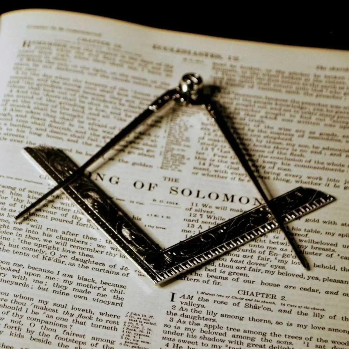 A ring made of a ruler and a compass placed on an open Bible, specifically on the pages of the Book of Solomon.