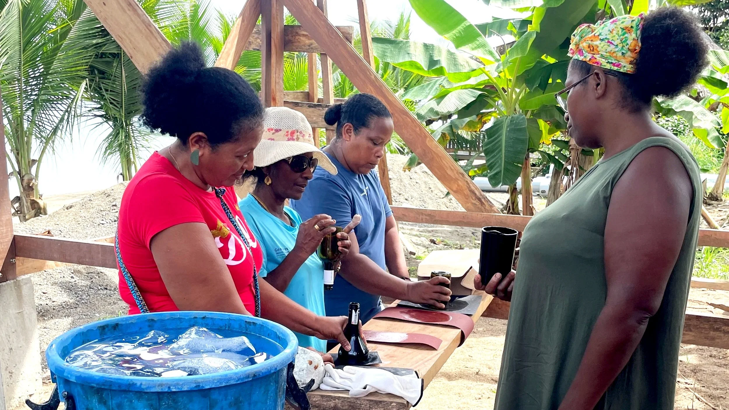 Cuatro mujeres en una construcción, revisando frascos y documentos, al aire libre con palmeras y vegetación tropical.