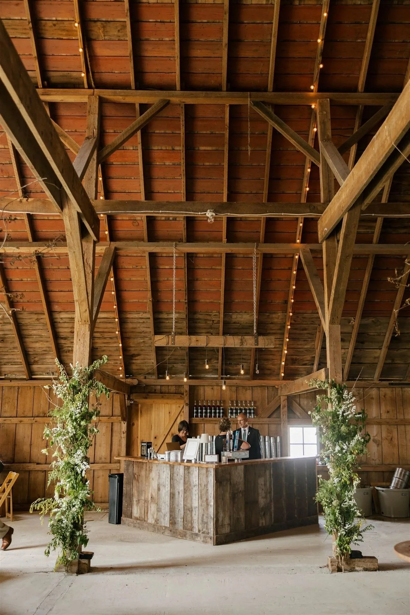 rustic bar, floral climbing up wooden beams, lights hanging over bar, guests mingling.