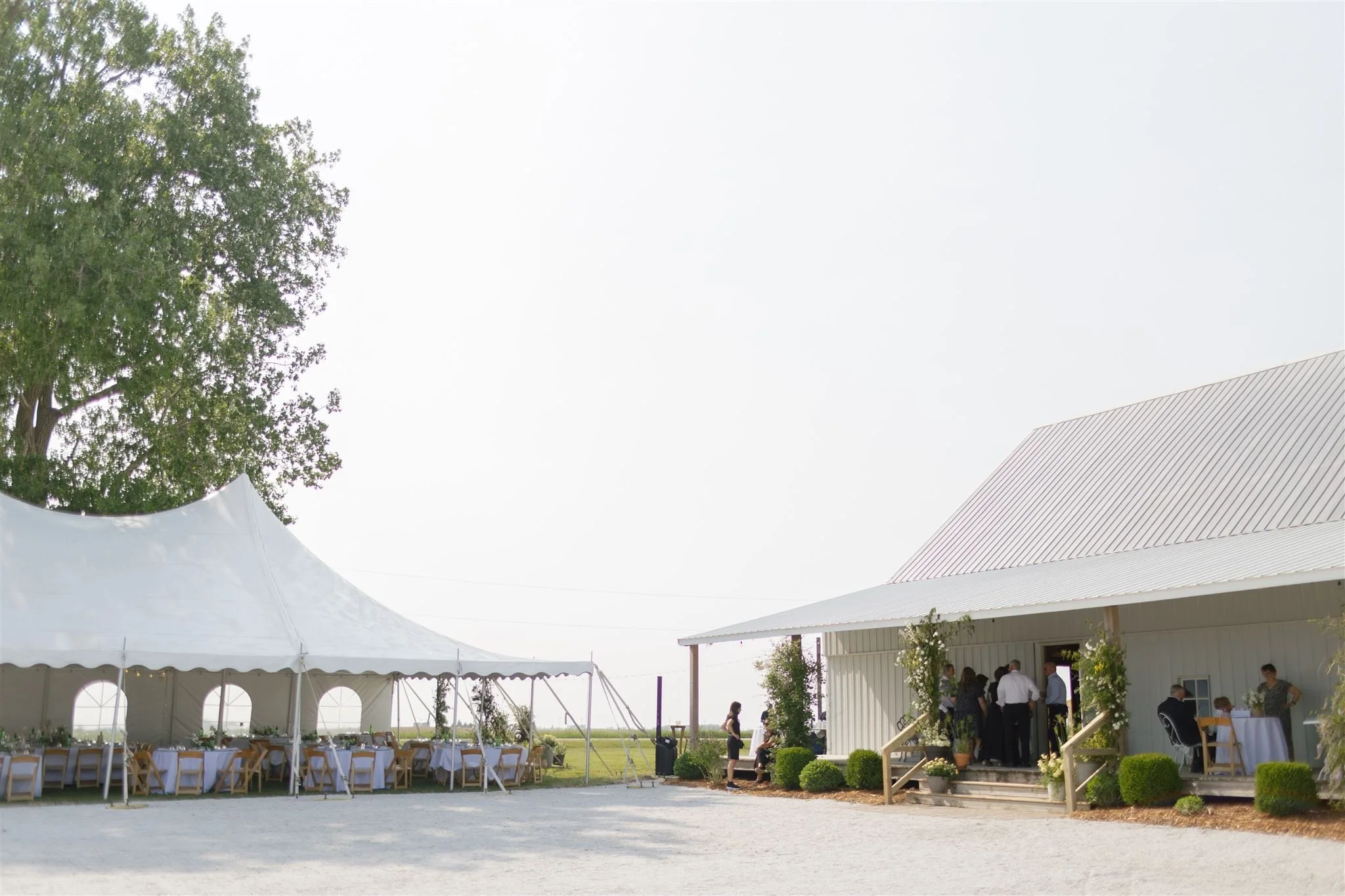 Wedding reception outdoor setup, tent, long tables, guests gathering porch