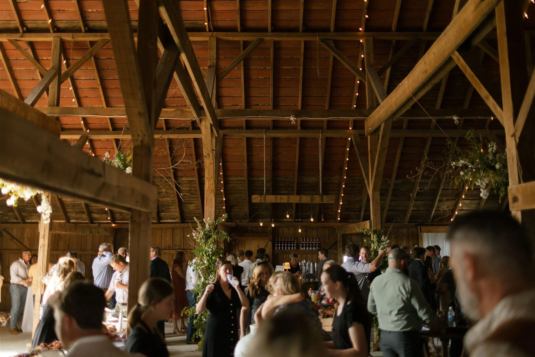 People socializing, rustic barn. wooden beams, string lights, drinks, laughing guests.