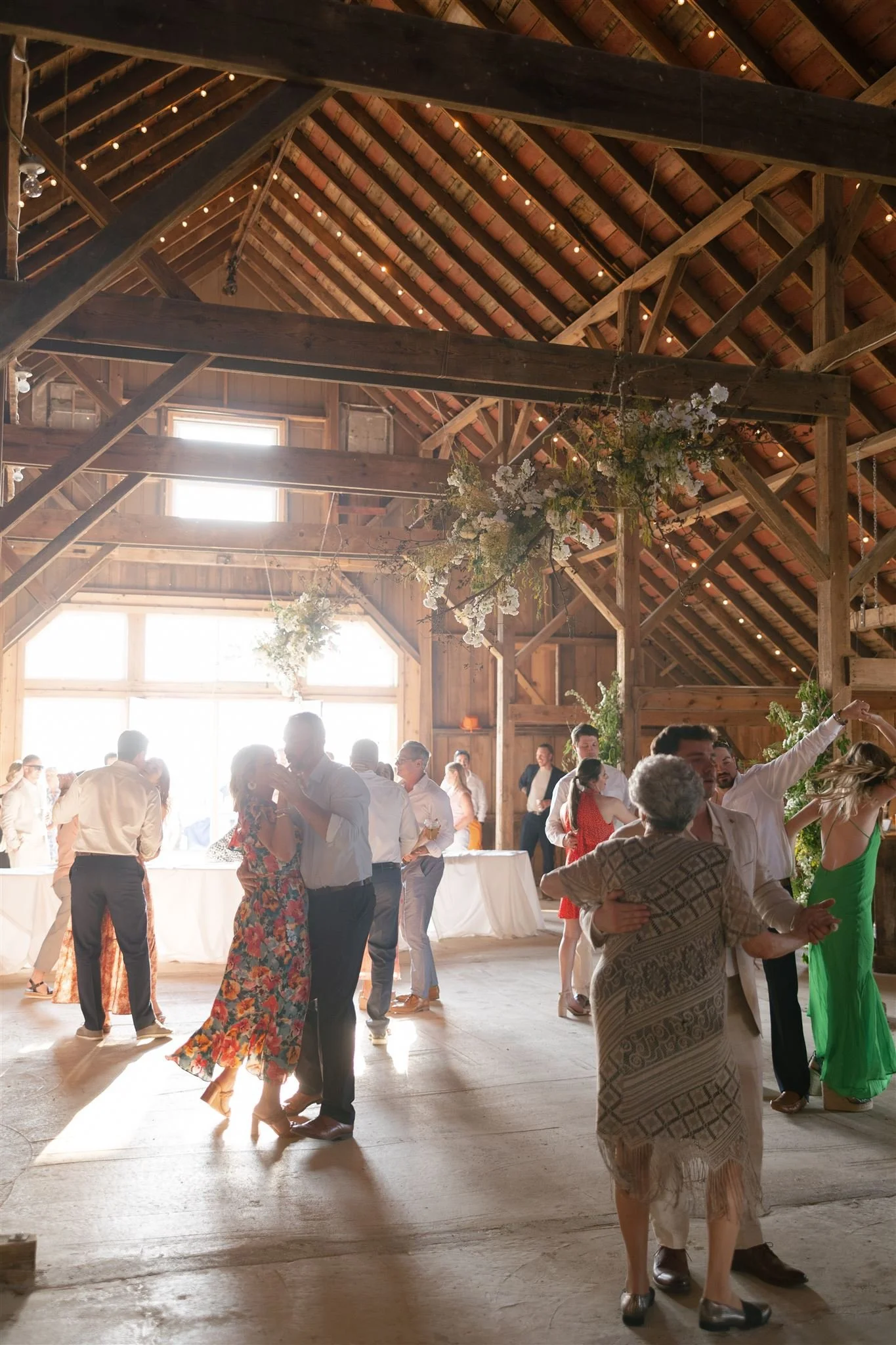 People dancing in rustic barn, wooden beams, flower decorations, wedding reception.