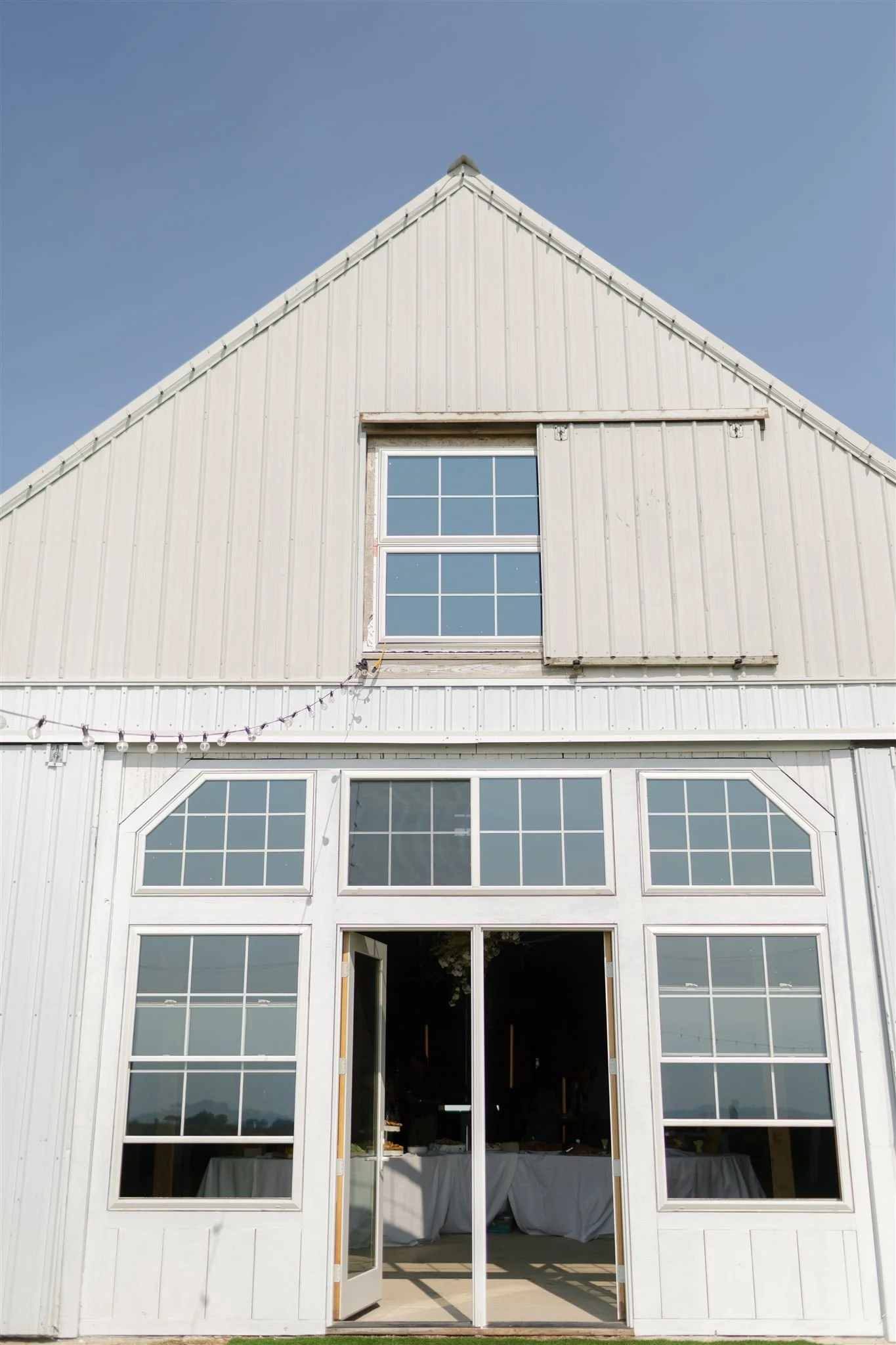 White barn-style building, large glass windows, sliding door, blue sky.