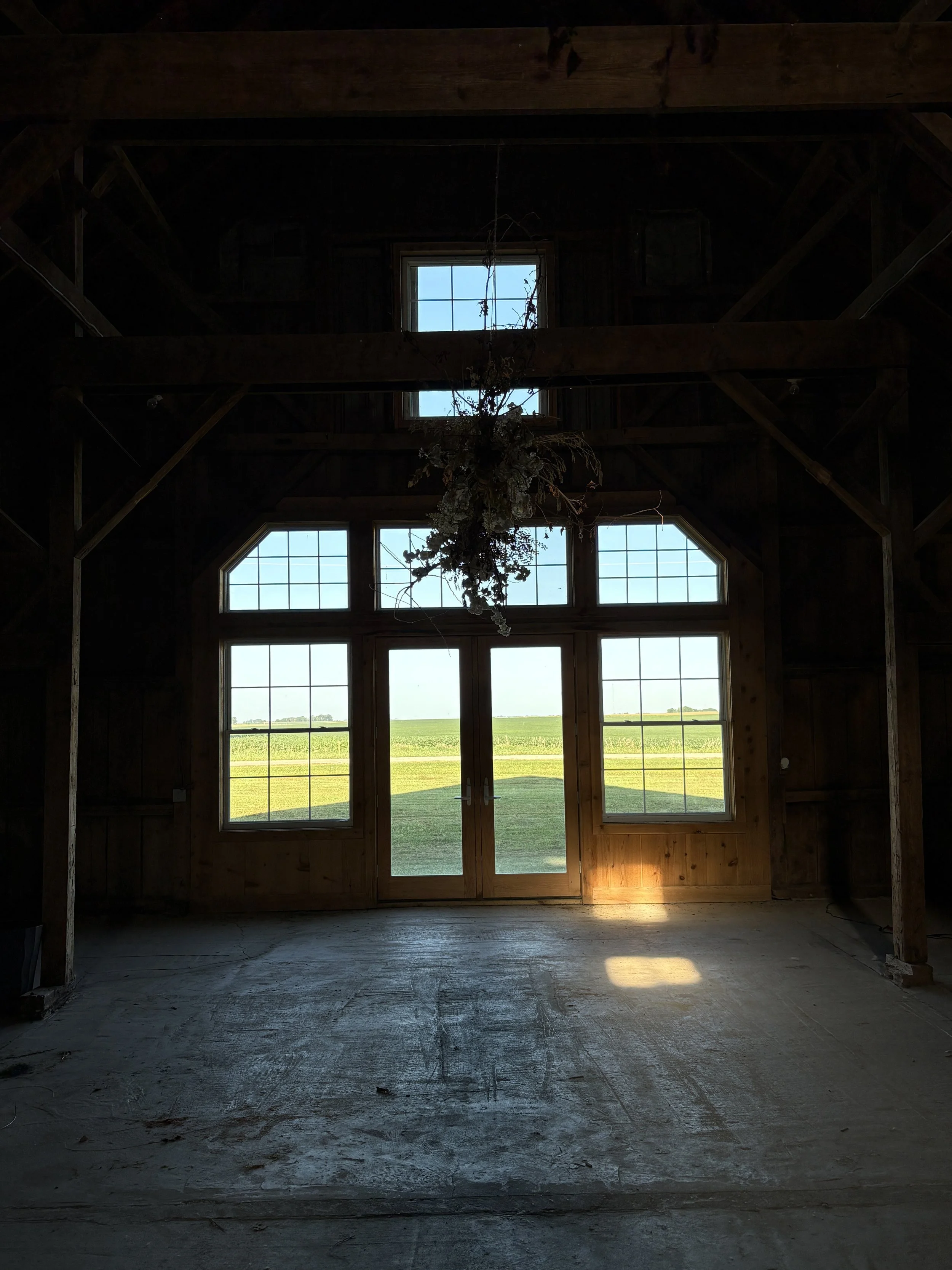 Inside the large white barn, empty, facing west, large windows, double doors.