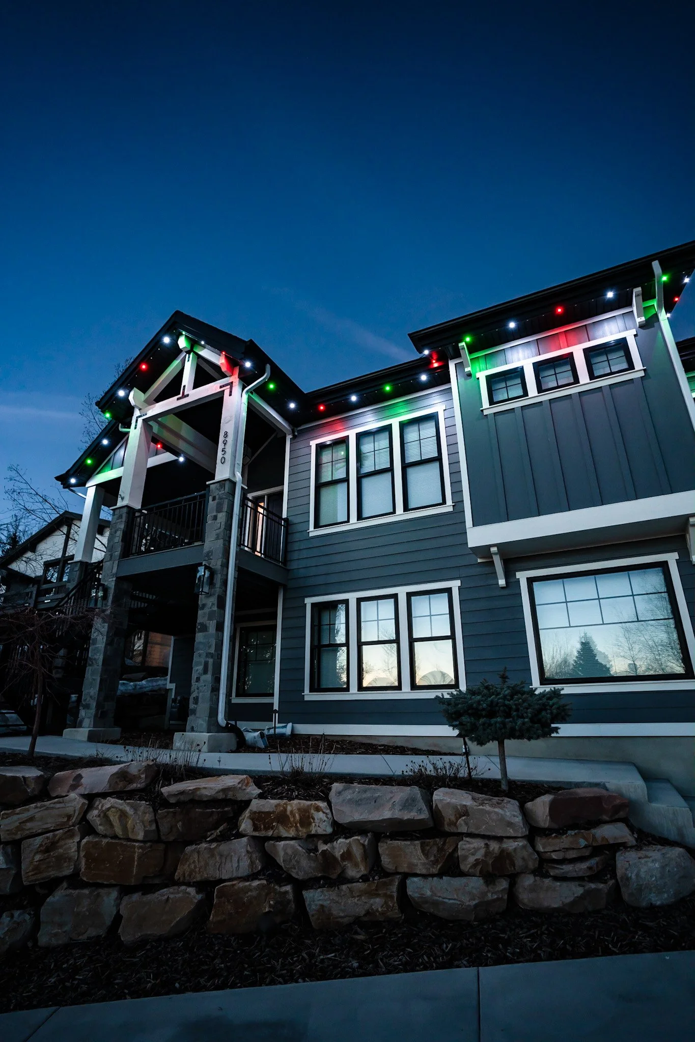 A modern two-story house decorated with colorful Christmas lights during dusk with a clear sky.