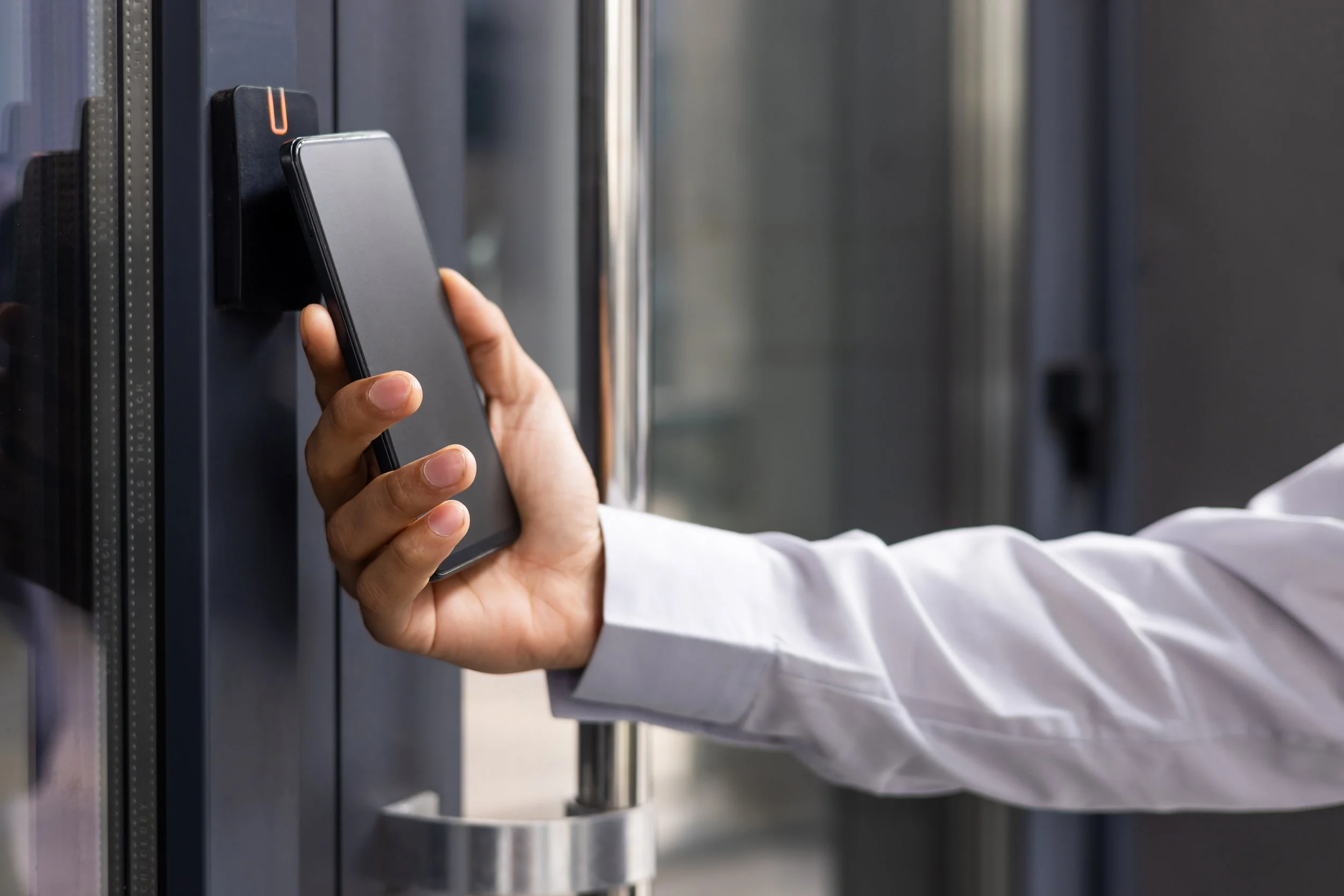 Person using a smartphone with a contactless payment terminal on a glass door.