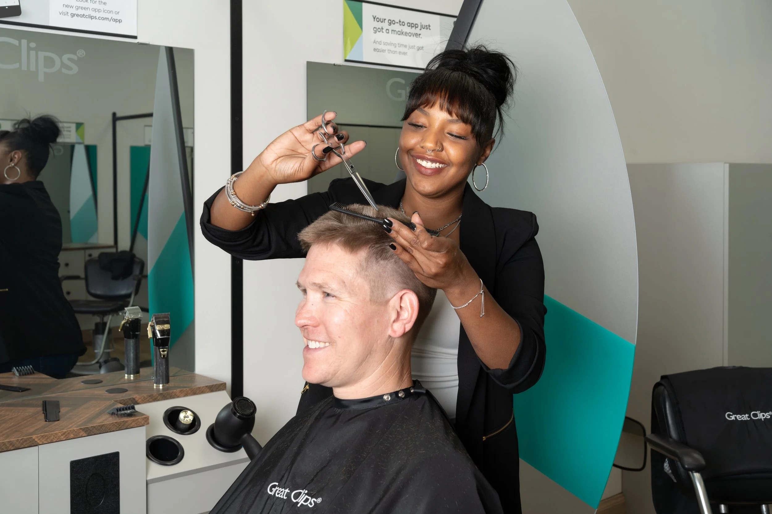 A woman getting a haircut at a salon, smiling while the hairstylist cuts her hair.