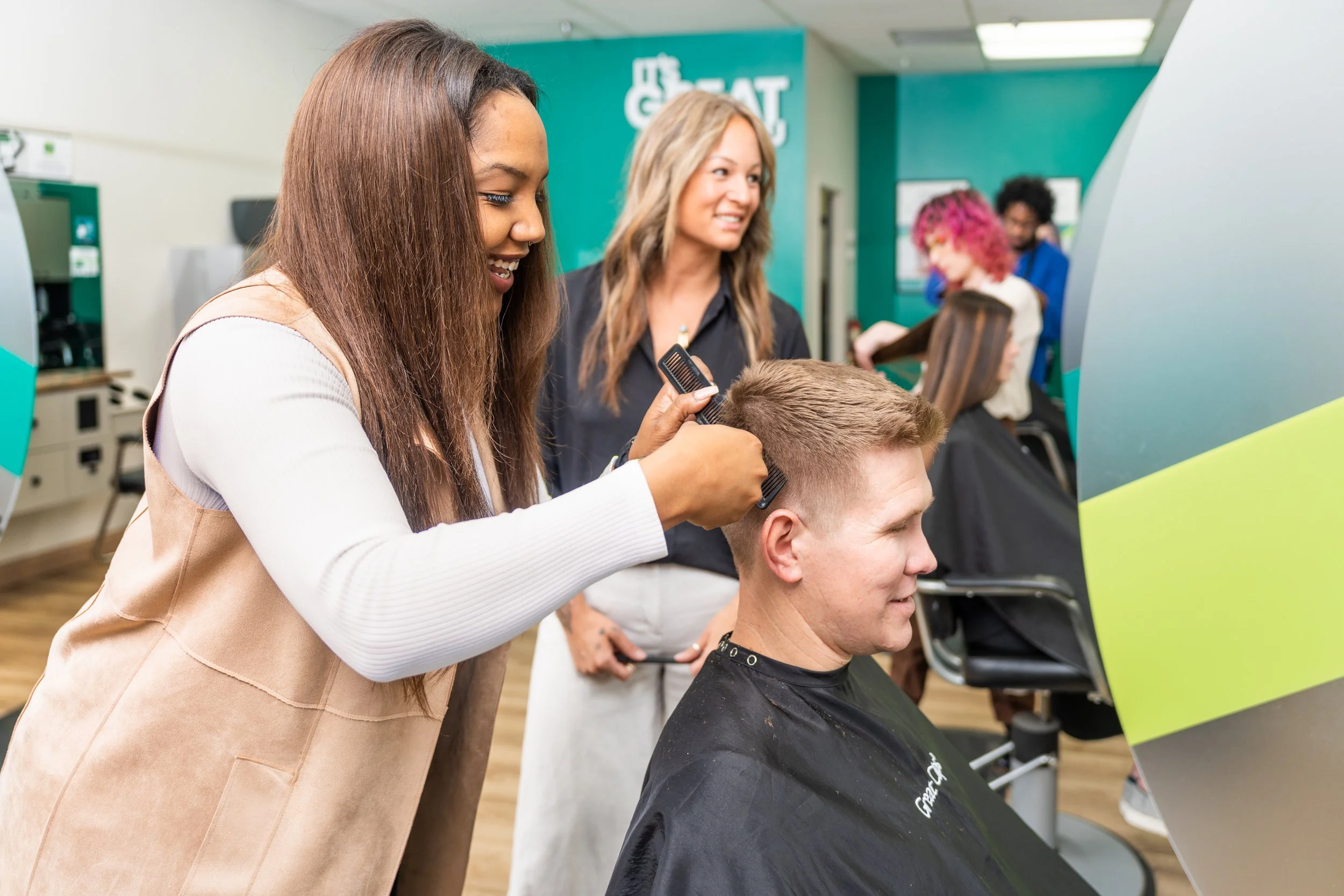 A woman getting a haircut at a salon, with two women in the background engaging with clients.