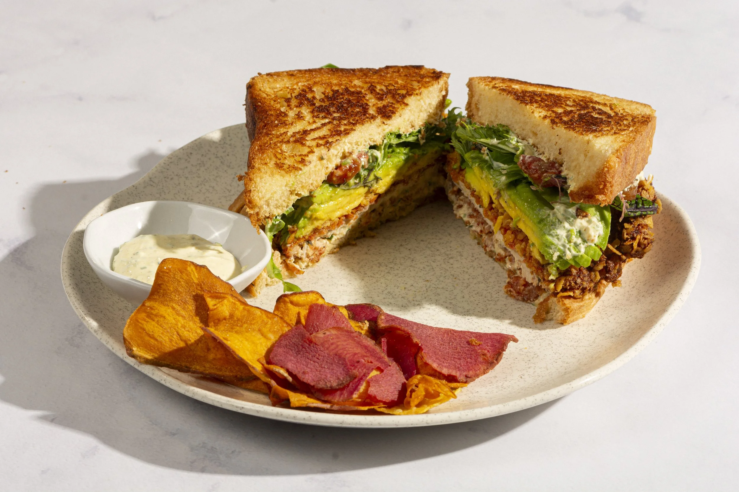 Sánduche en pan brioche suave y recién horneado, con ranch artesanal de la casa, aguacate, mezclum fresco y tomates caramelizados. Coronado con pollo crocante apanado en Doritos para una explosión de sabor y textura. Acompañado de chips de vegetales.