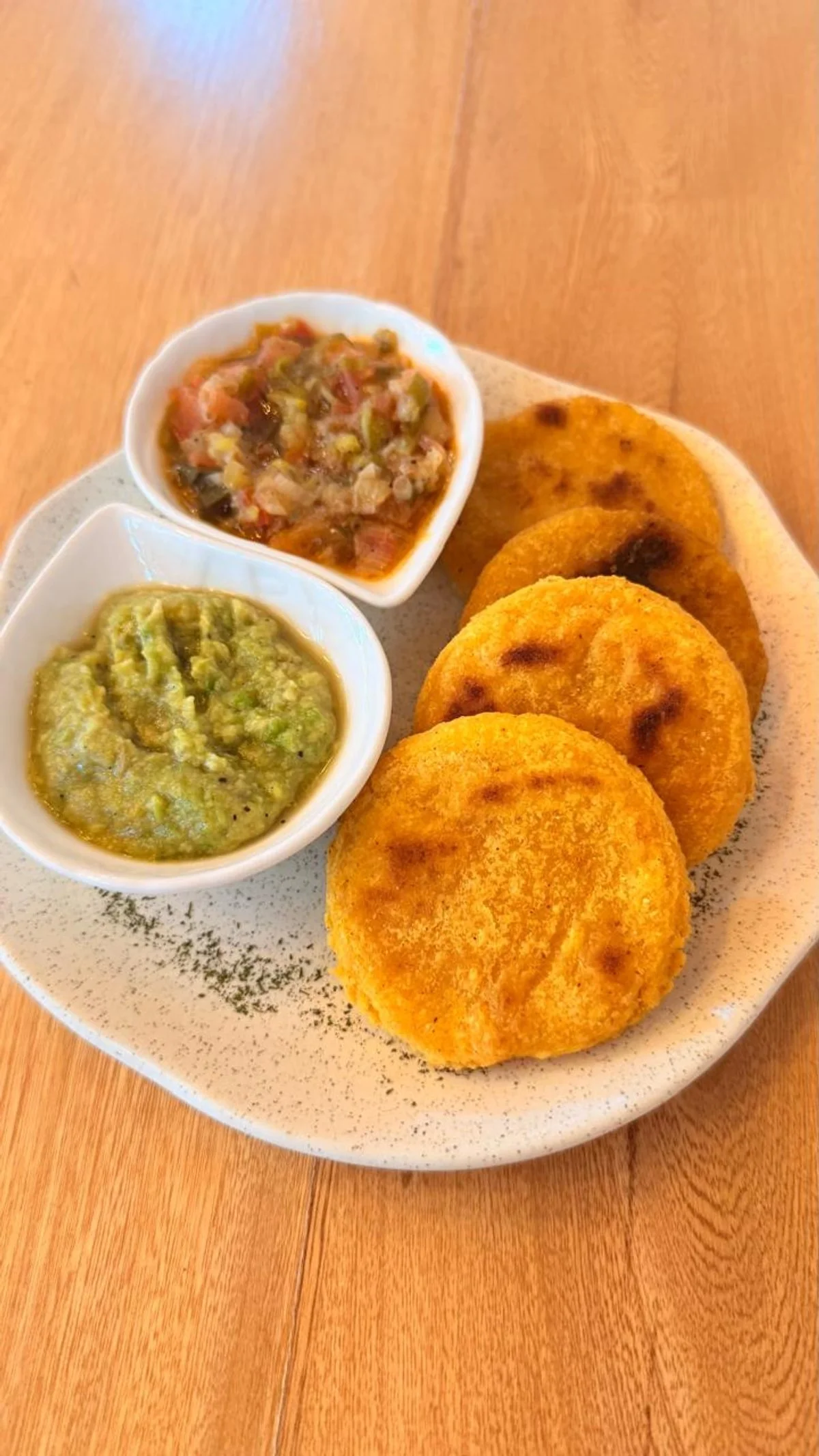 Plato con cuatro pupusas doradas acompañadas de repollo y salsas