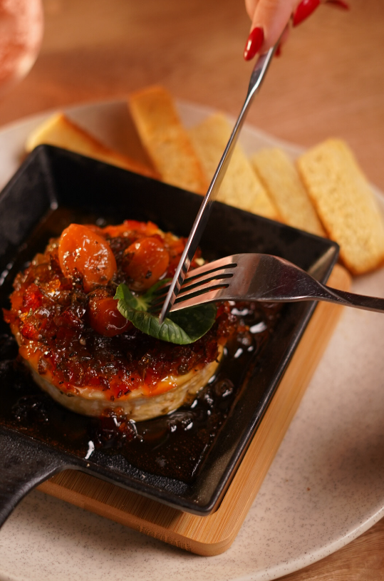 Plato de queso fundido con salsa de tomates y jalapeños, acompañado de rebanadas de pan y tortillas.