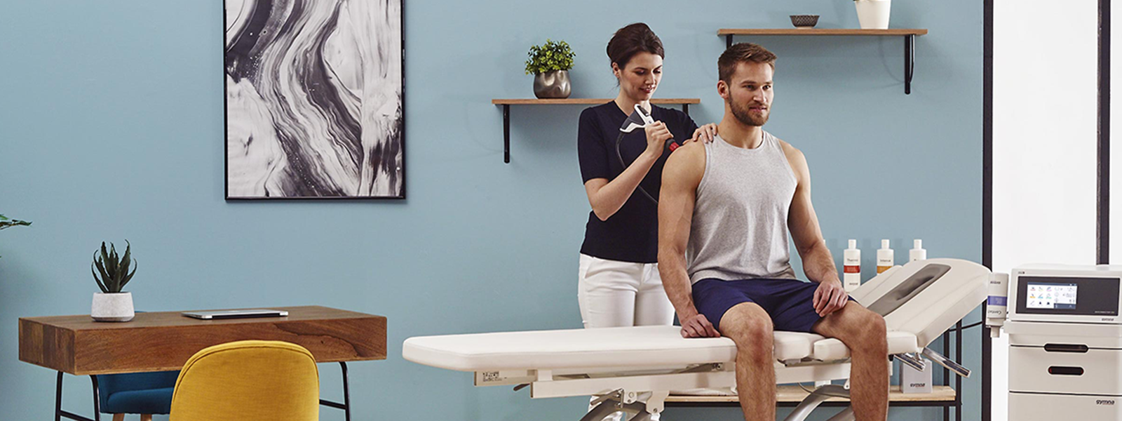 A man sitting on an examination table in a medical examination room with a healthcare professional applying ultrasound gel to his shoulder.