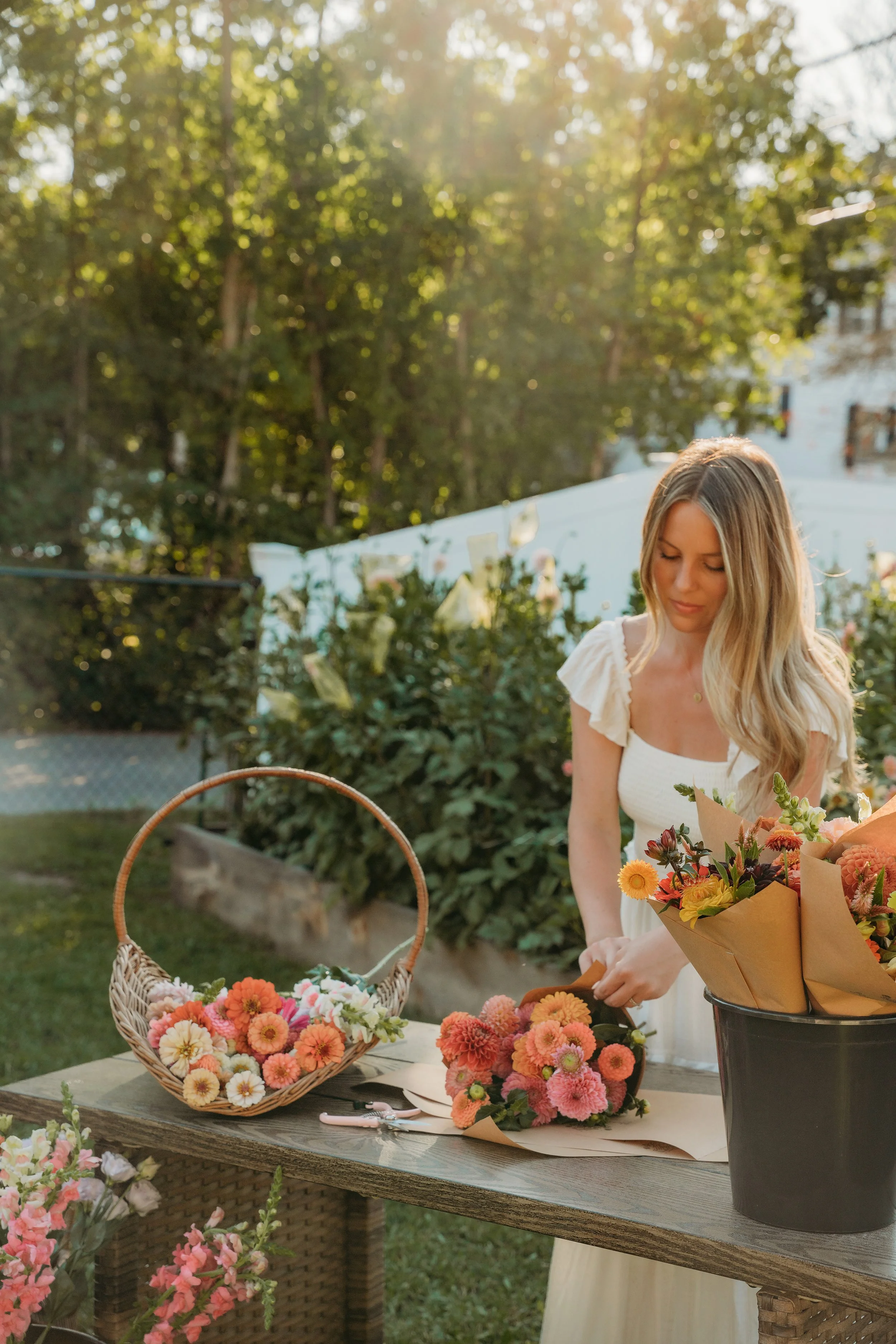 A woman arranging colorful flowers in a garden during sunset.
