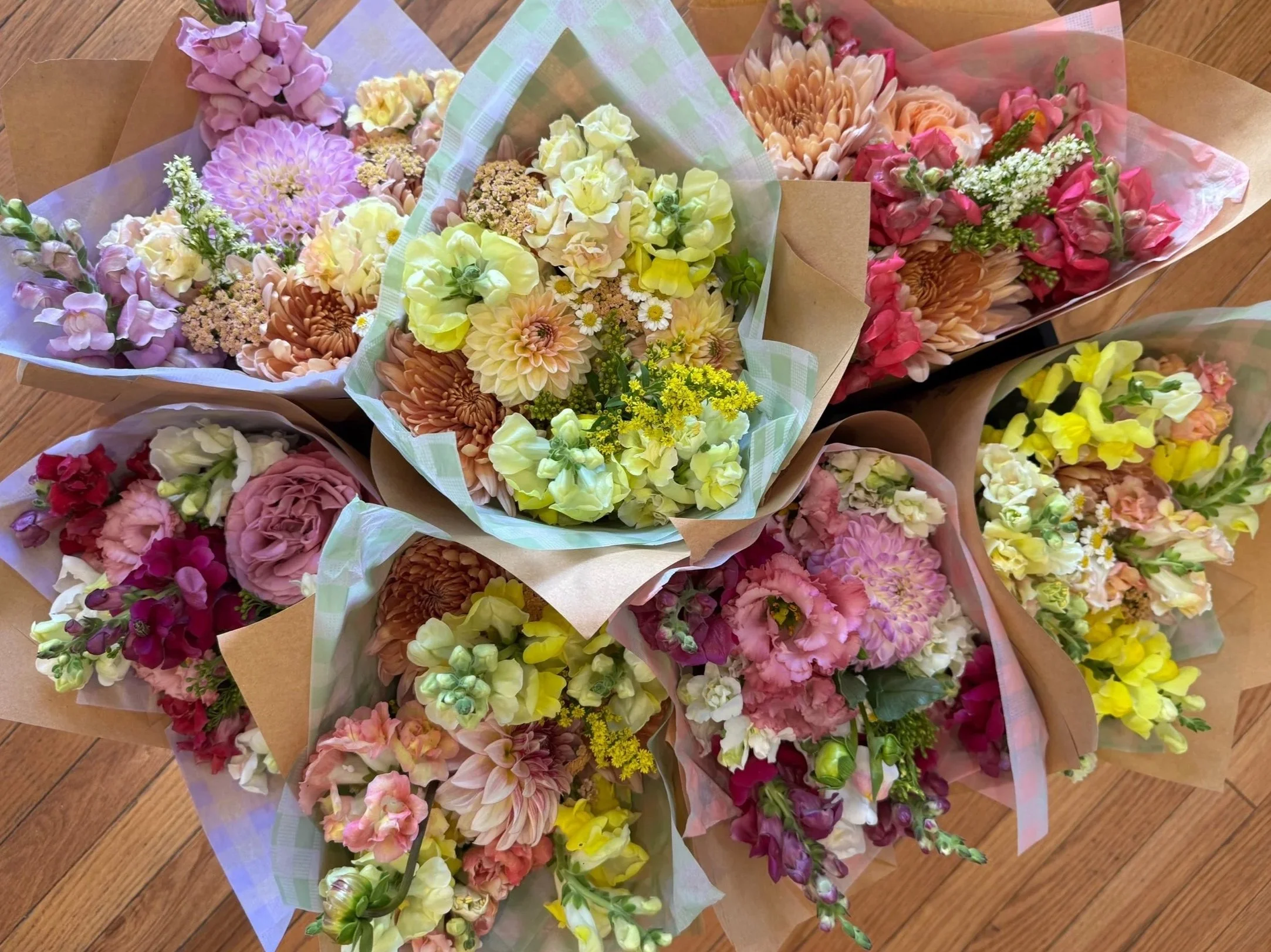 Three bouquets of pink and purple flowers wrapped in brown paper, placed on a wooden floor.