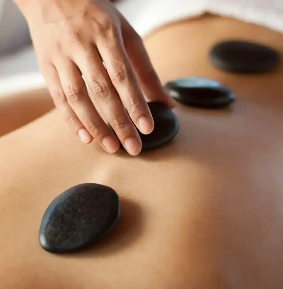 Close-up of a person placing flat black stones on a person's back forHot stone massage therapy.