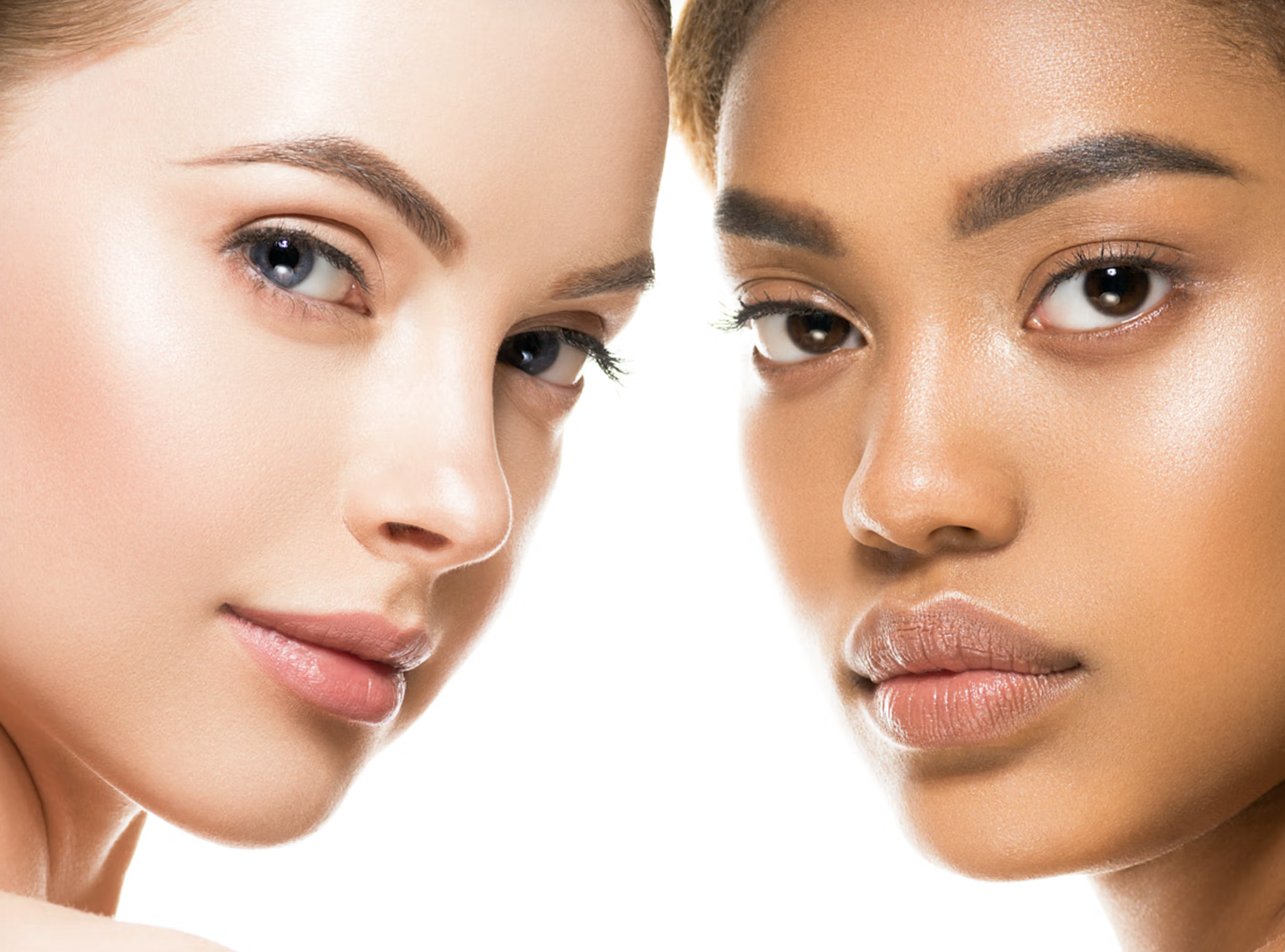 Close-up of two women with different skin tones and eye colors looking at the camera, with makeup and clear skin.
