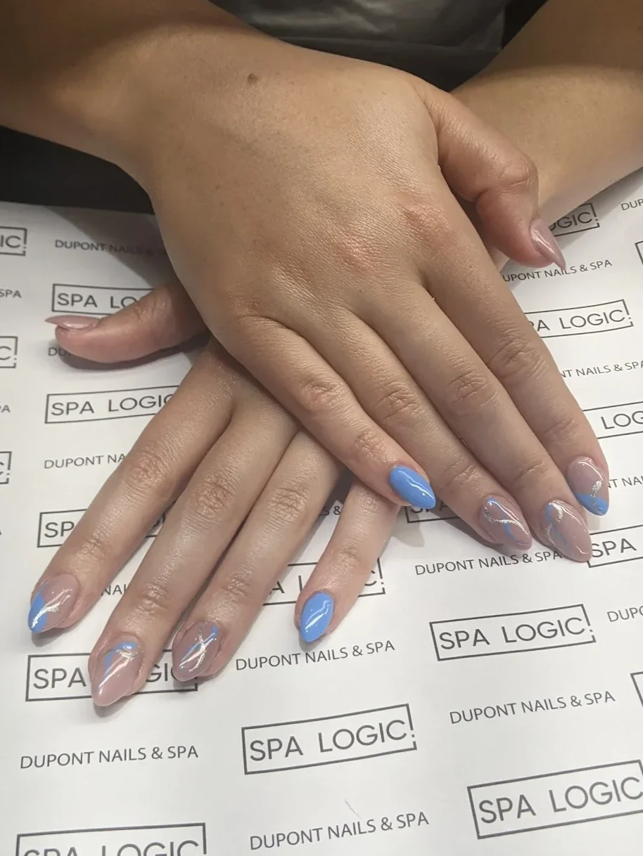 Close-up of hands with manicured nails, one hand resting on the other, with blue and clear nail polish with silver accents, in a spa setting, on paper labeled "Spa Logic" and "Dupont Nails & Spa."