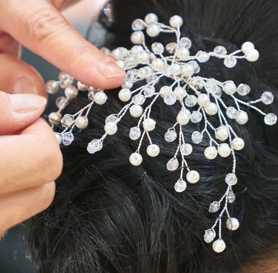 Close-up of a person pinning a decorative hair accessory with pearl and crystal beads to dark hair.