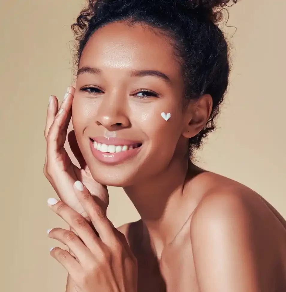 A woman with curly hair smiling and showing her teeth, with a small white heart sticker on her cheek.