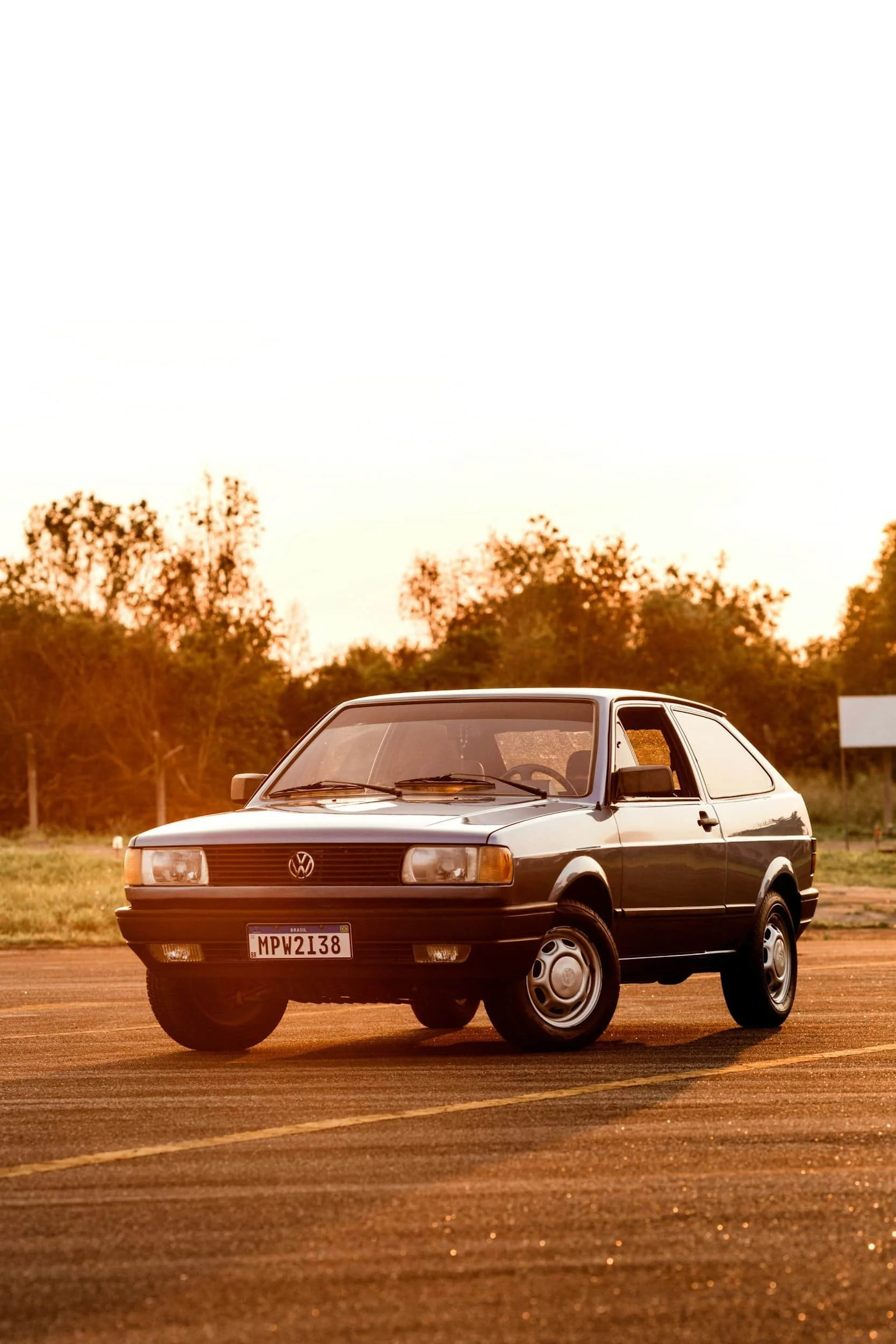 A classic black Volkswagen car parked in an open area during sunset with trees in the background.