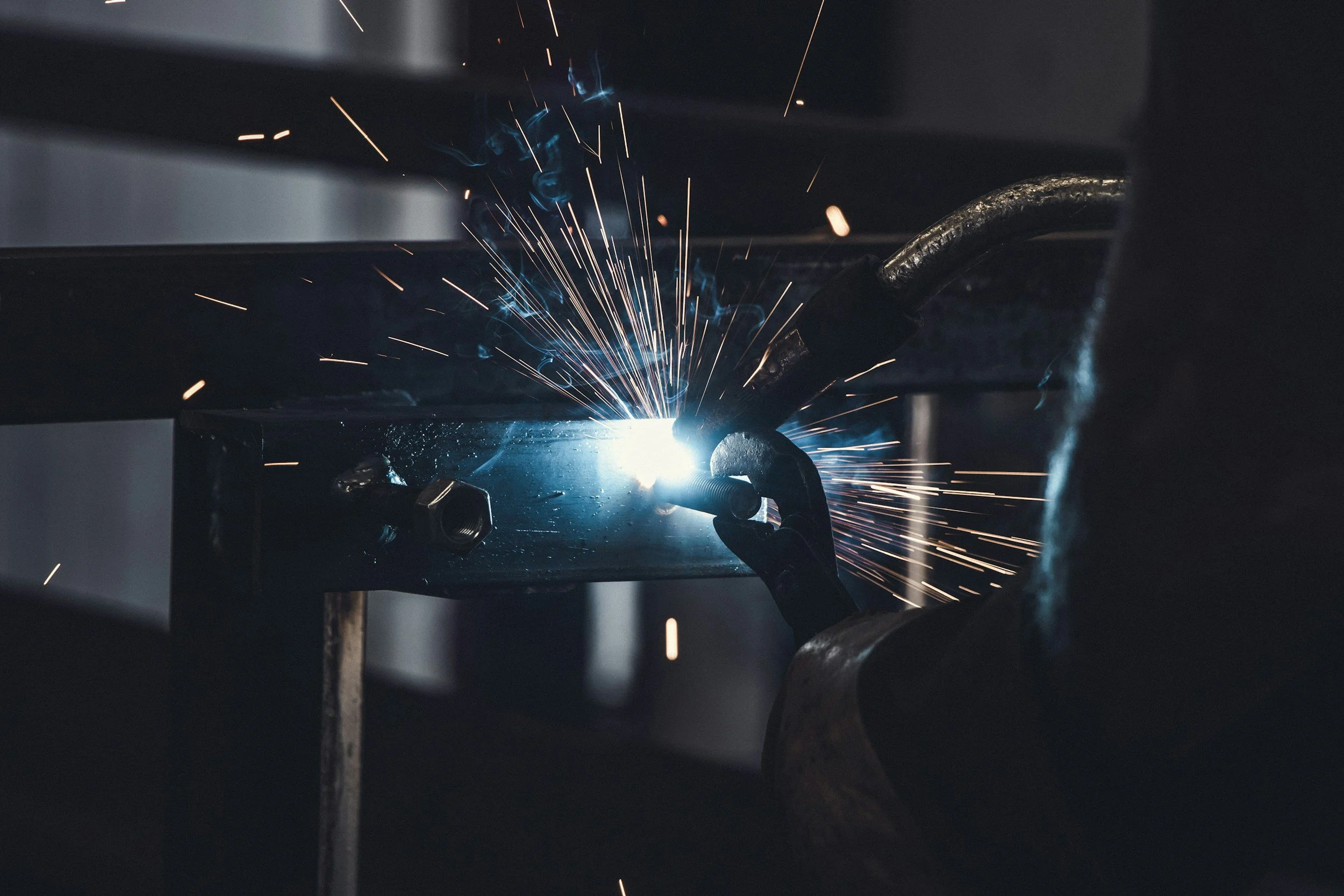 A worker welding metal, with sparks flying in an industrial setting.