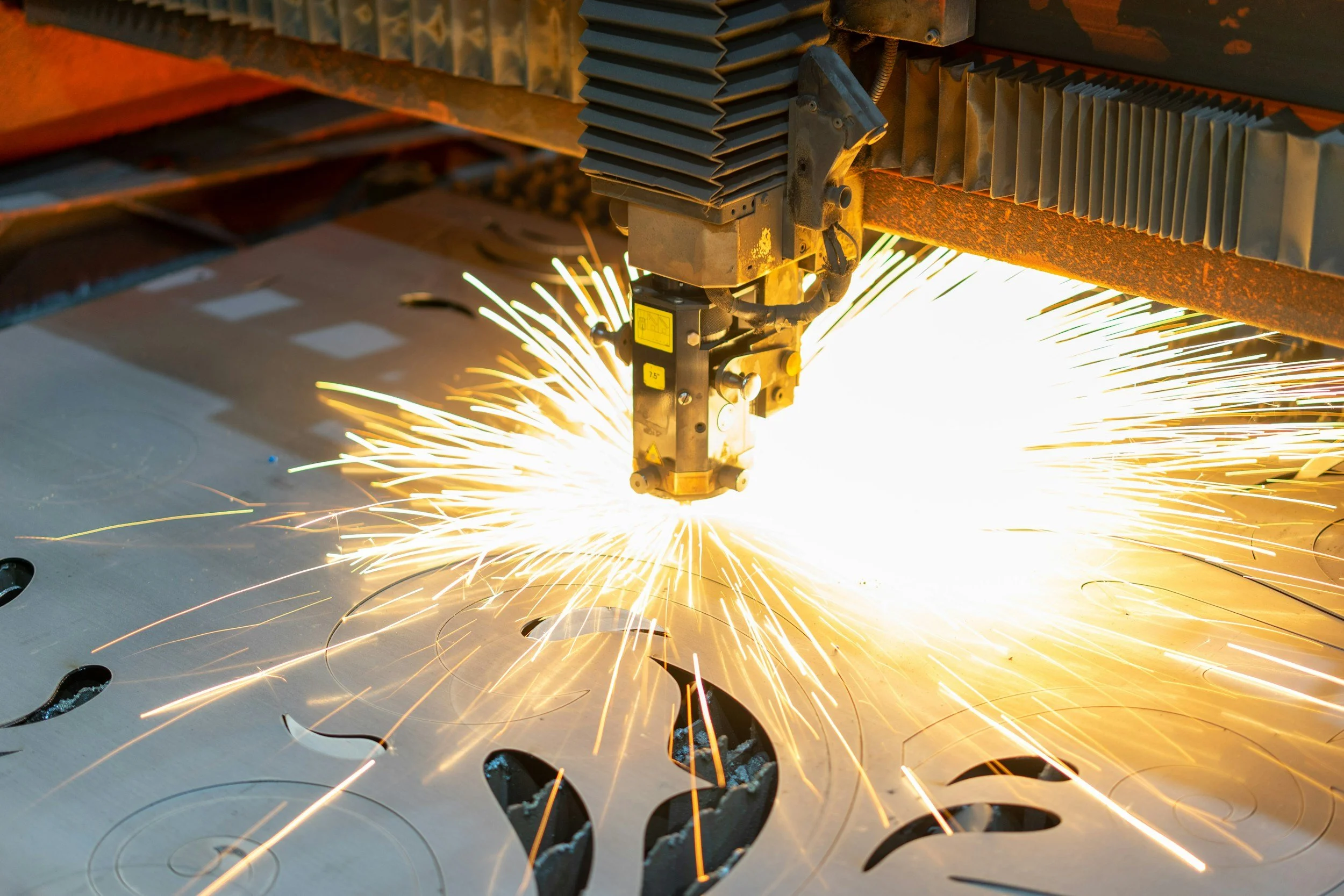 A laser cutter machine cutting a design into metal, with sparks flying.