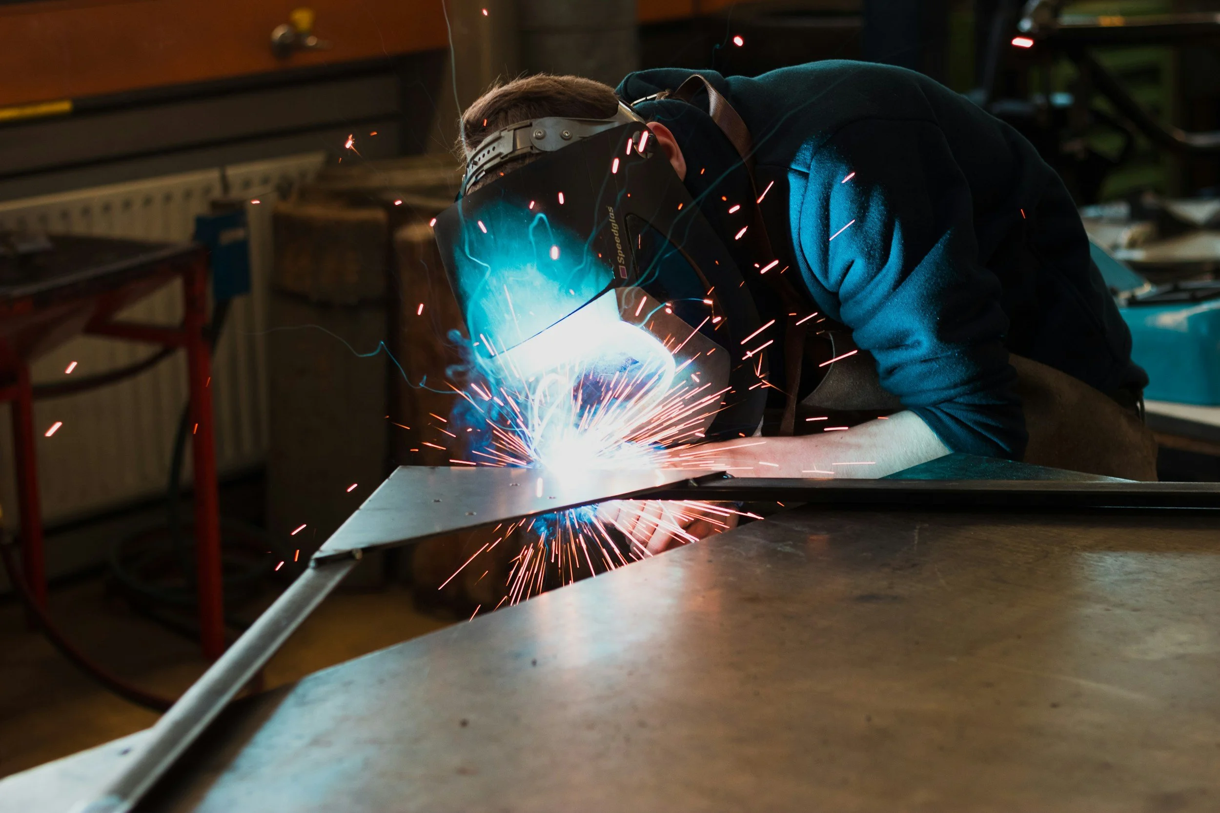 Person welding metal in a workshop with sparks flying.