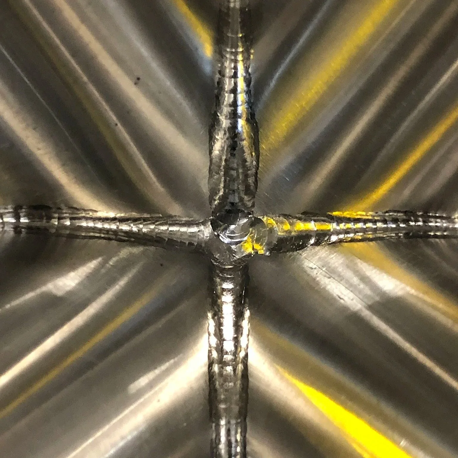 Close-up view of a aerospace titanium weld joint where four metal pieces meet at a central point.