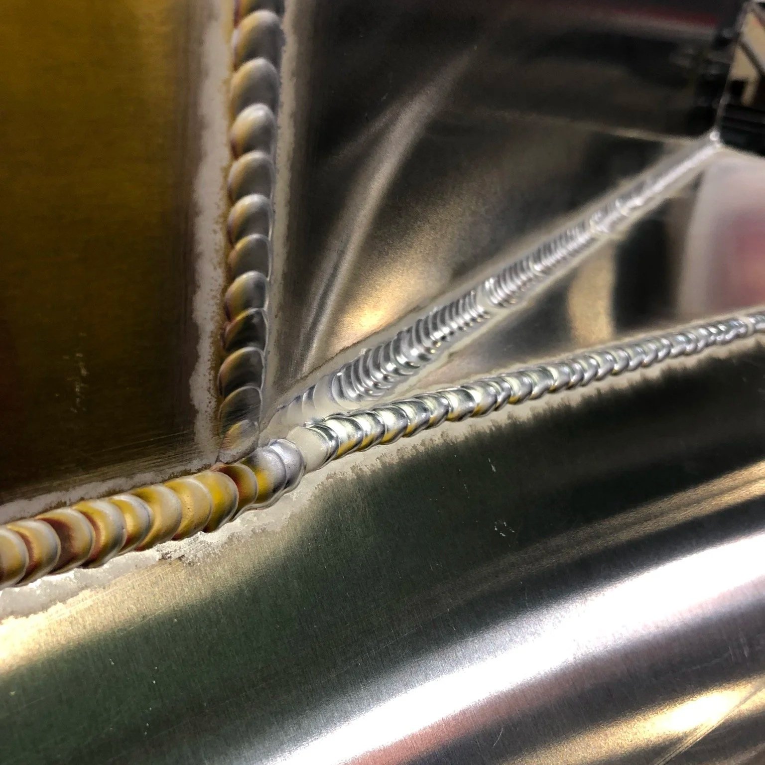 Close-up of a metal welding seam showing two distinct weld beads on a stainless steel surface.
