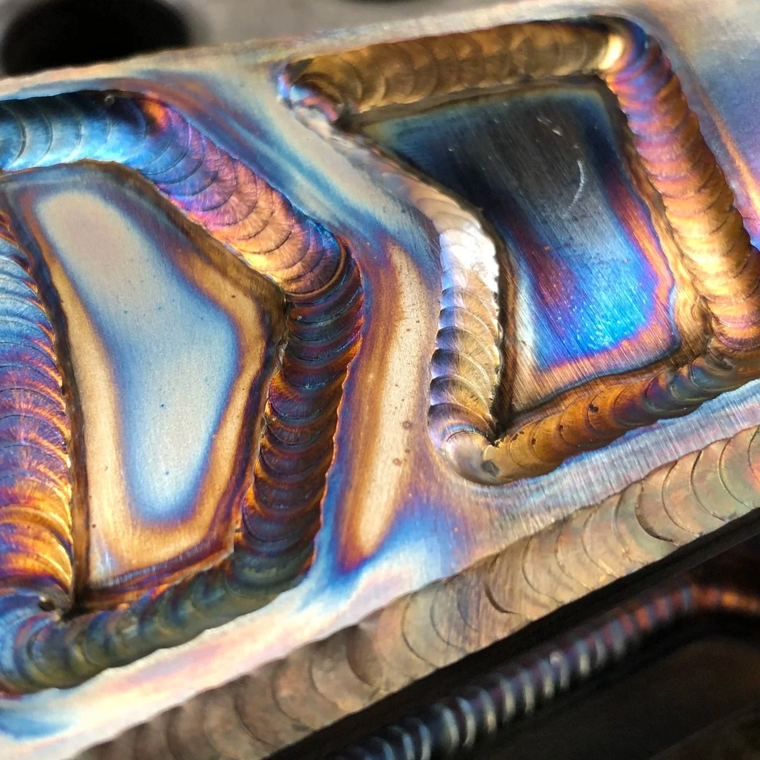 Close-up of a metal welding joint with rainbow-colored heat-affected zone patterns and weld beads.