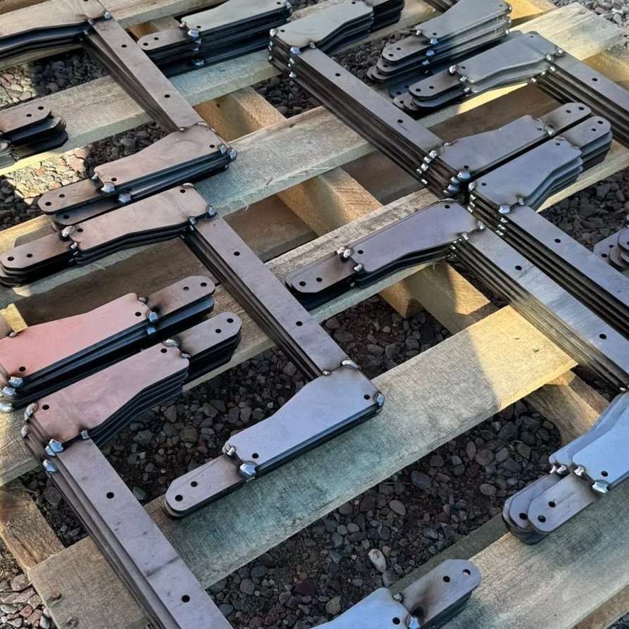 Stacked welded brackets brackets placed on a wooden pallet outdoors.