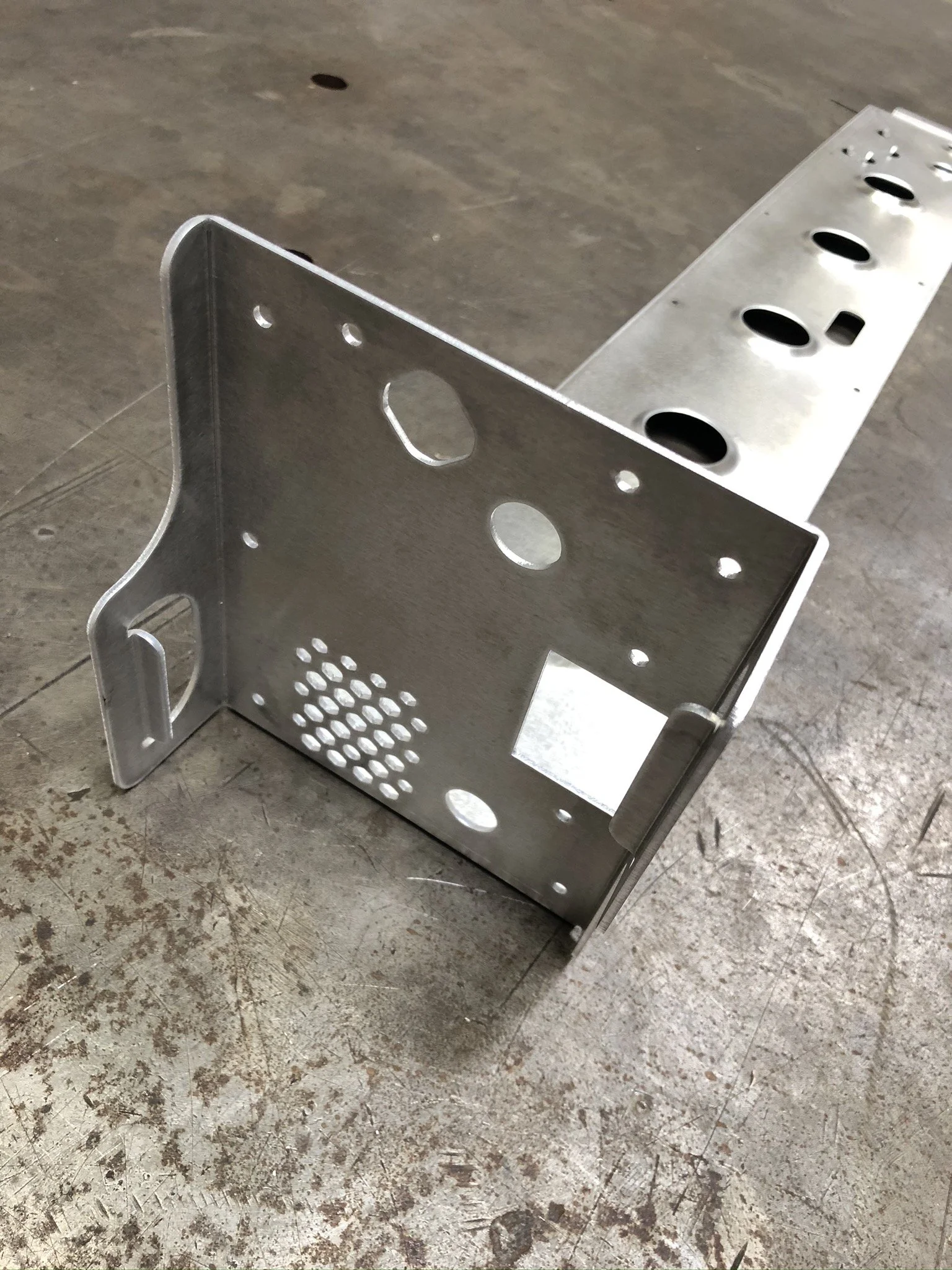 A cnc bent bracket or case on a concrete floor, with various holes and slots for components.