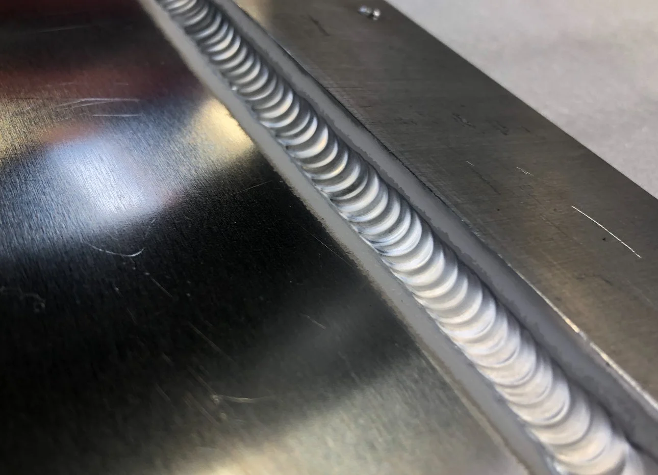 Close-up of a metal weld seam on a dark metallic surface.