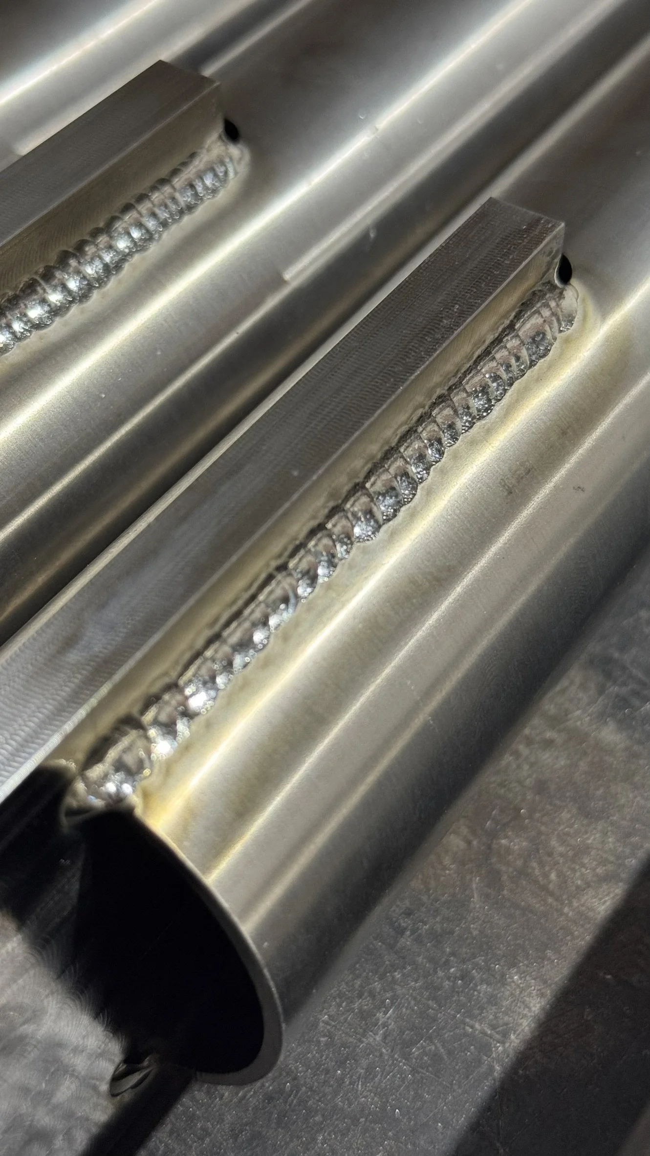 Close-up of a metal welding process on a stainless steel cylindrical object, showing a row of weld beads.