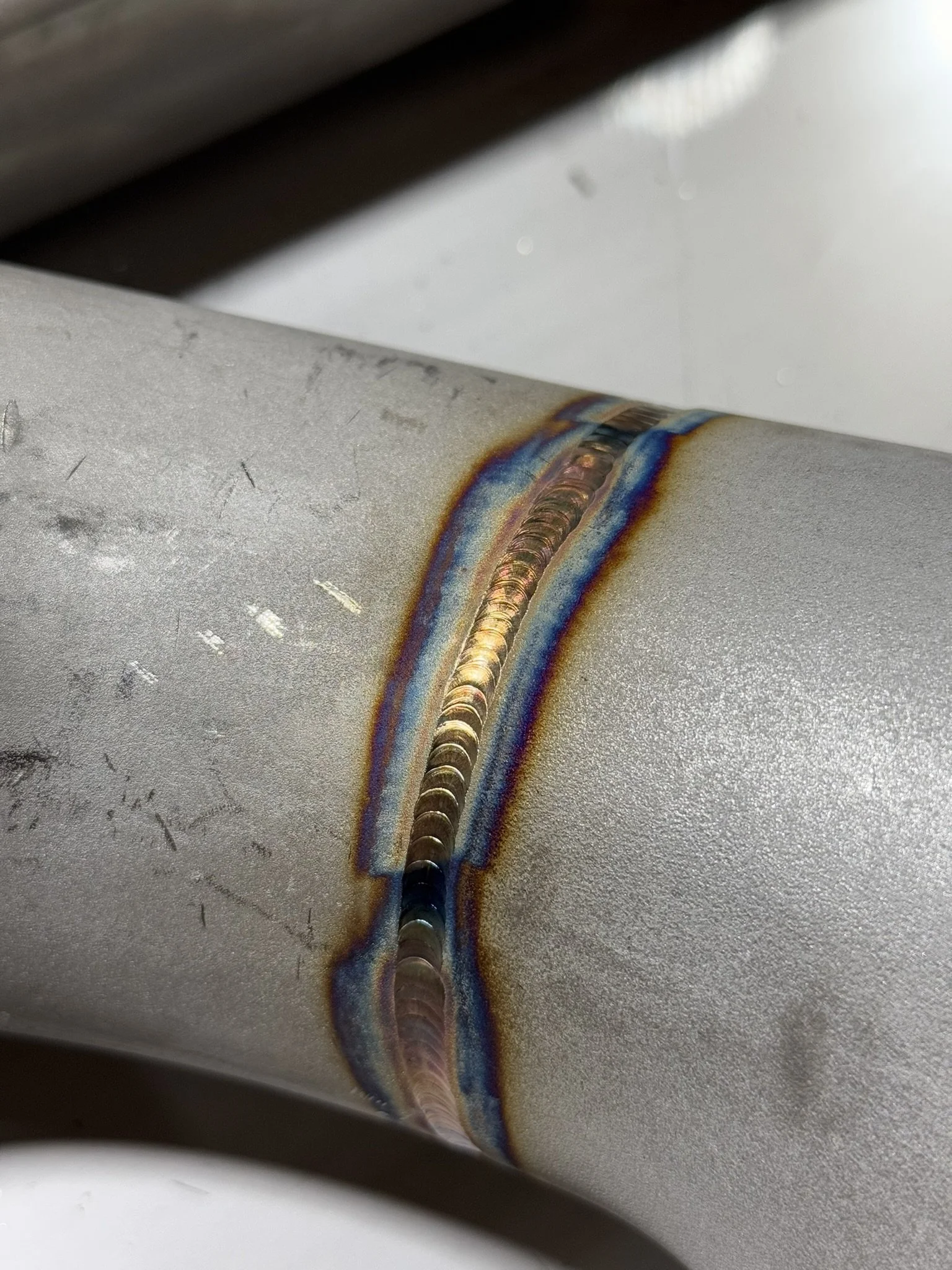 Close-up of a stainless steel metal pipe with a weld seam, showing heat discoloration and weld beads along the joint.