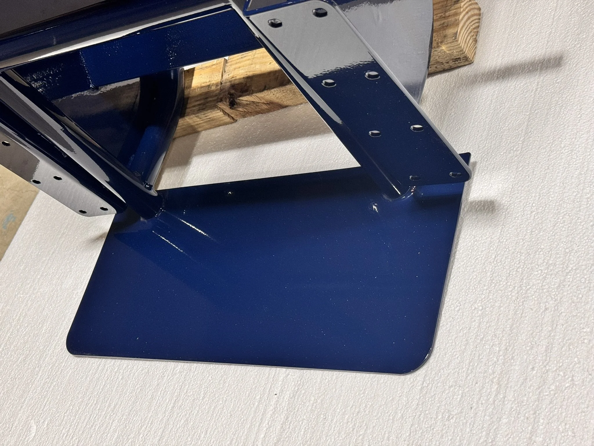 Close-up of a blue metal stand with a flat base and vertical supports, placed on a textured white surface, with wooden blocks supporting the stand.