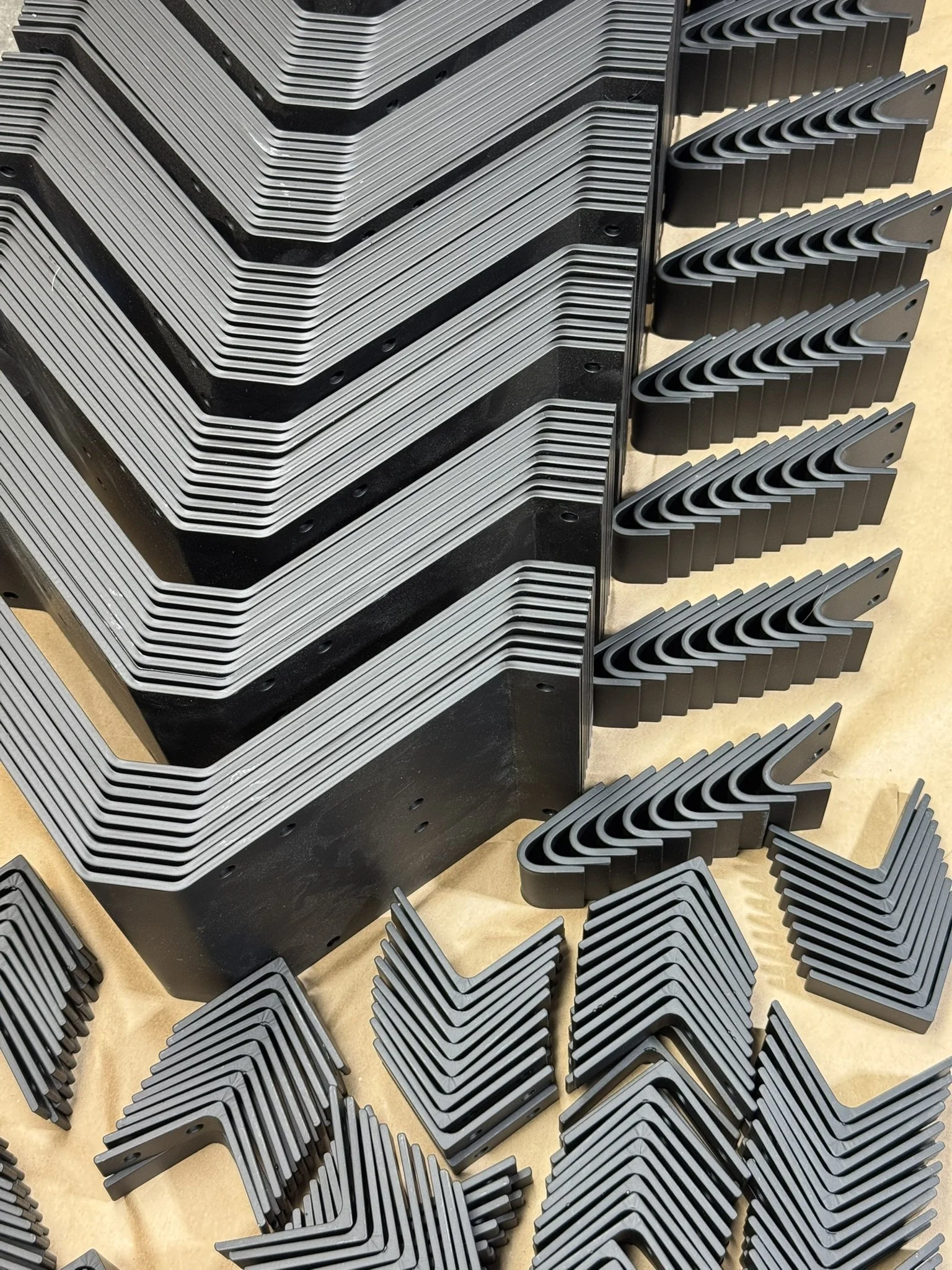 Powder coated brackets and L-shaped pieces arranged neatly on a light-colored surface.