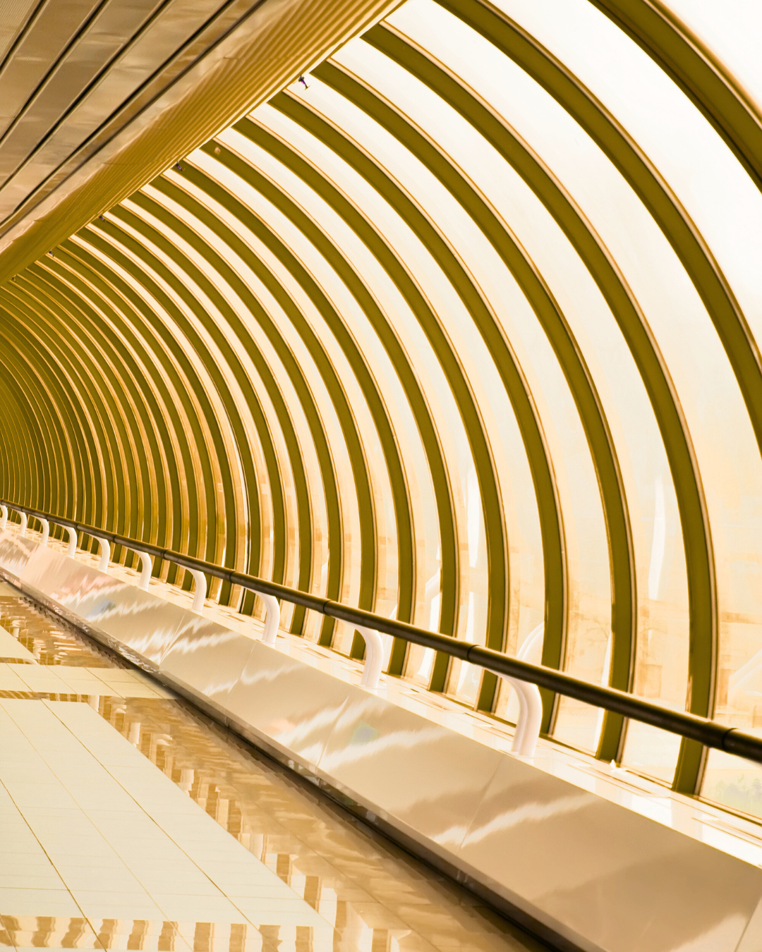 An empty tunnel with arched yellow and black stripes and a reflective tiled floor.