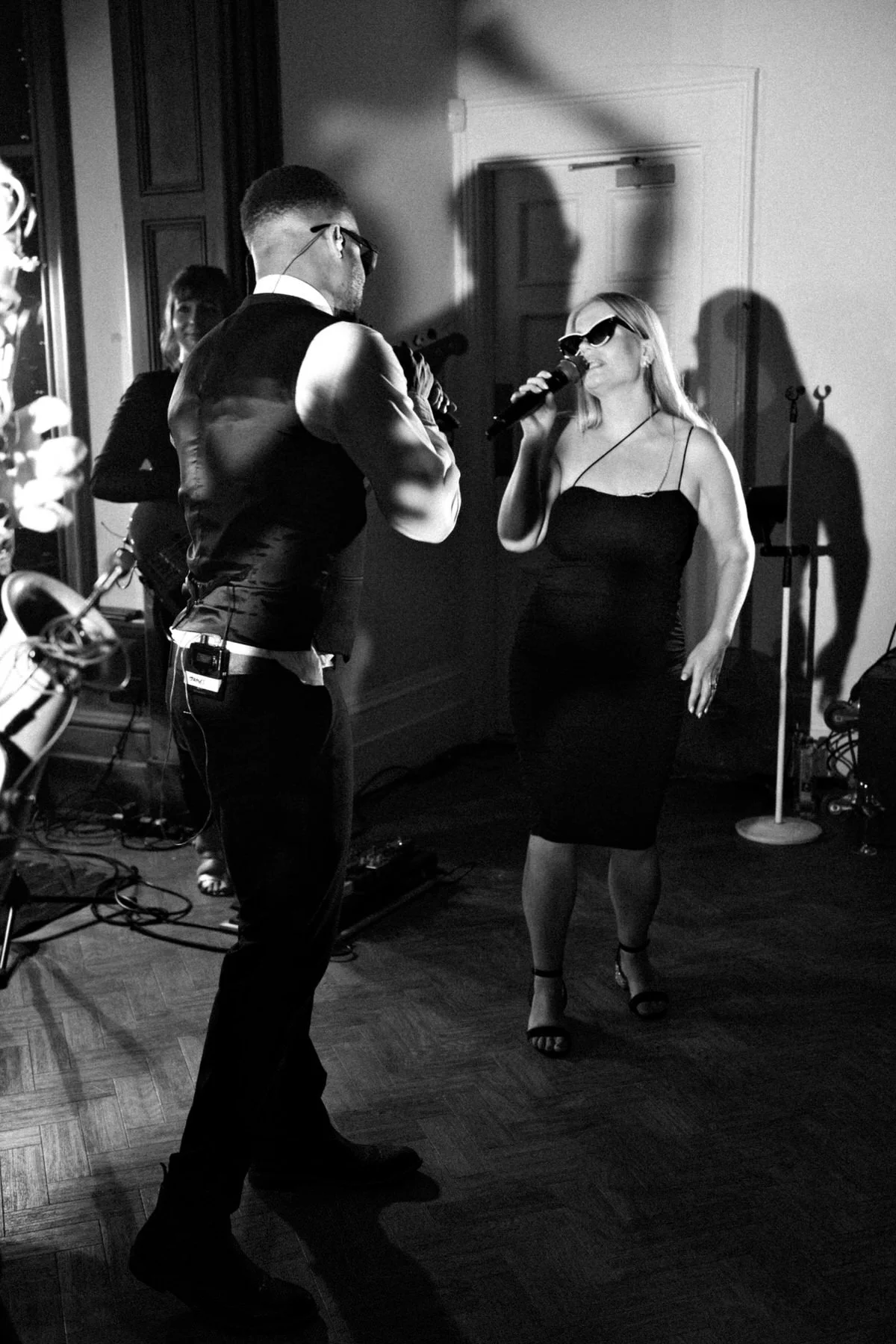 Black-and-white live performance: a male singer faces a woman in a fitted dress as they sing into microphones, creating an intimate mood.