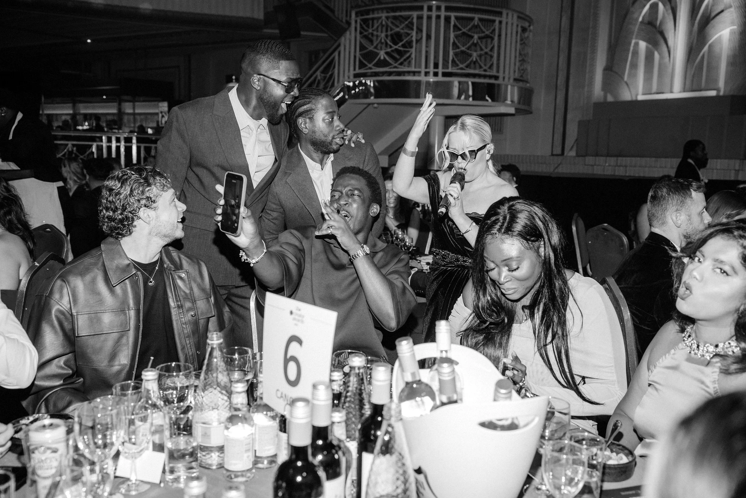 NeoRoots singer performs among guests at a London awards dinner as attendees film, sing and laugh during an energetic roaming performance.
