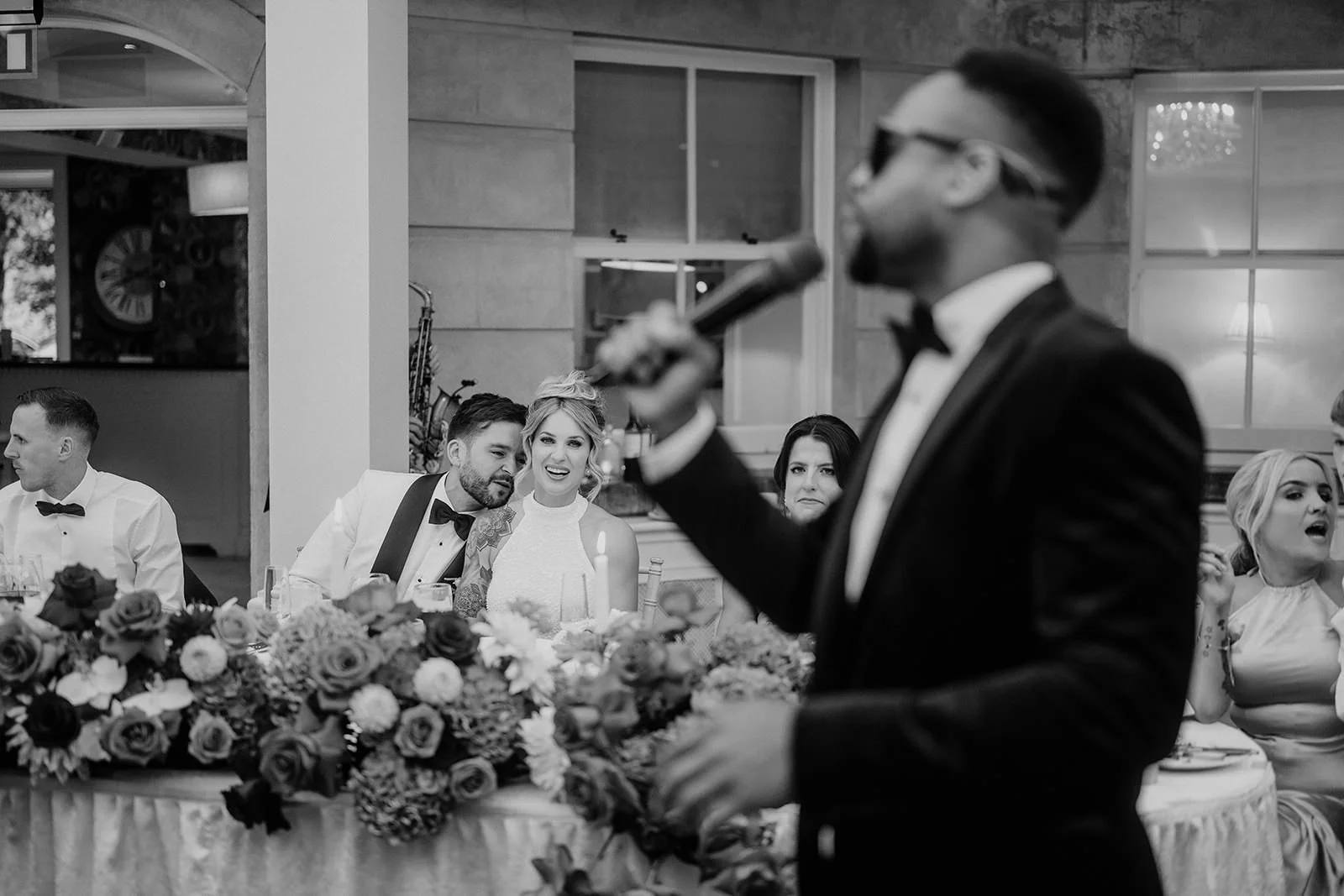 At Tankardstown House, Ireland, a NeoRoots singer in a tux performs as the bride and groom smile at their flower-lined table.