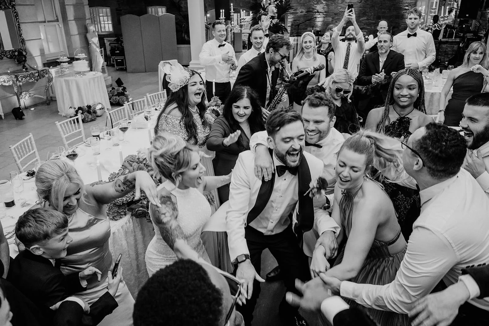 Guests crowd the dance floor, laughing and singing as NeoRoots perform, the bride and groom at the center of the joyful huddle.